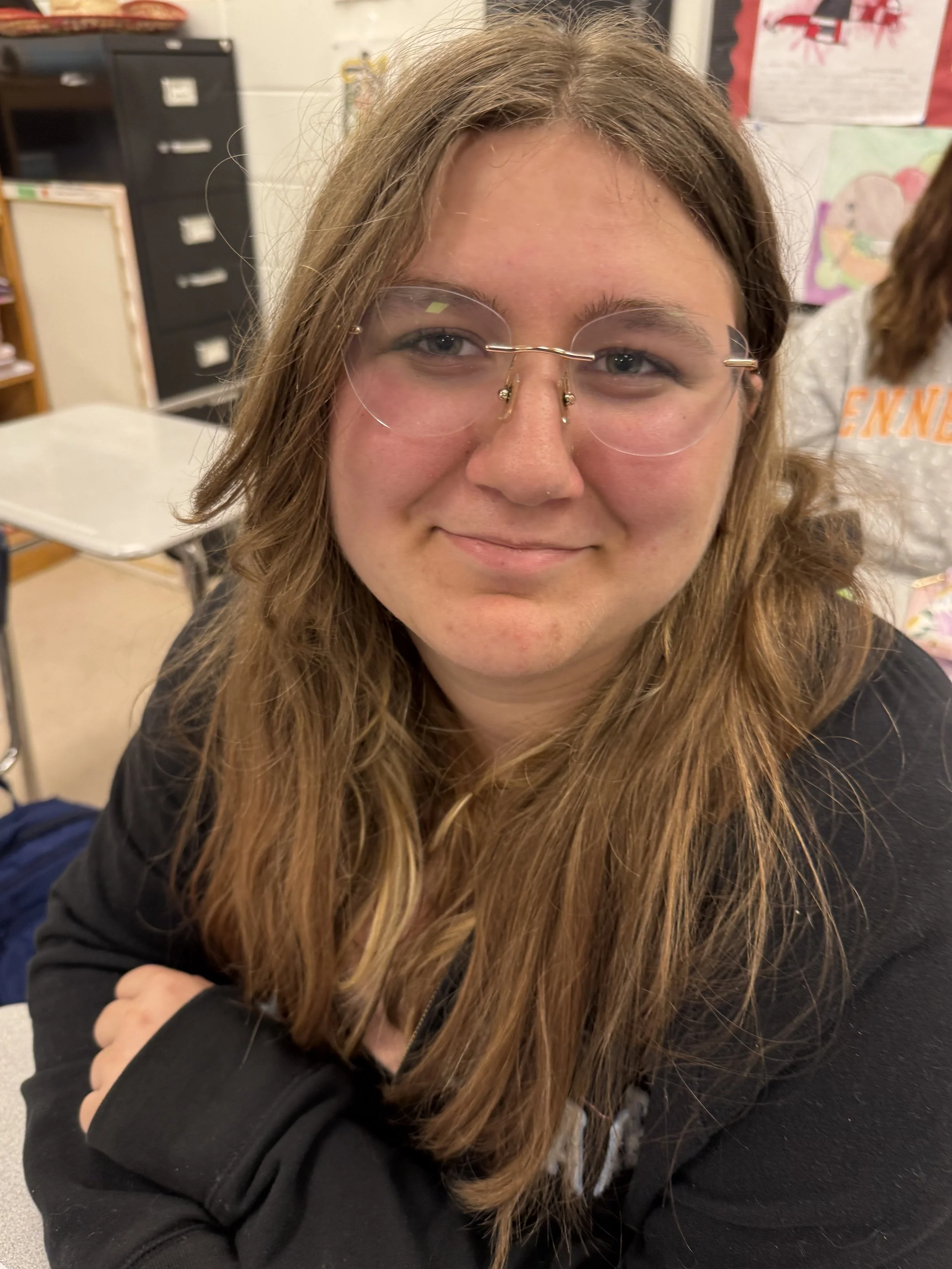 Close-up of a young woman wearing glasses, with a slight smile, in an indoor setting.