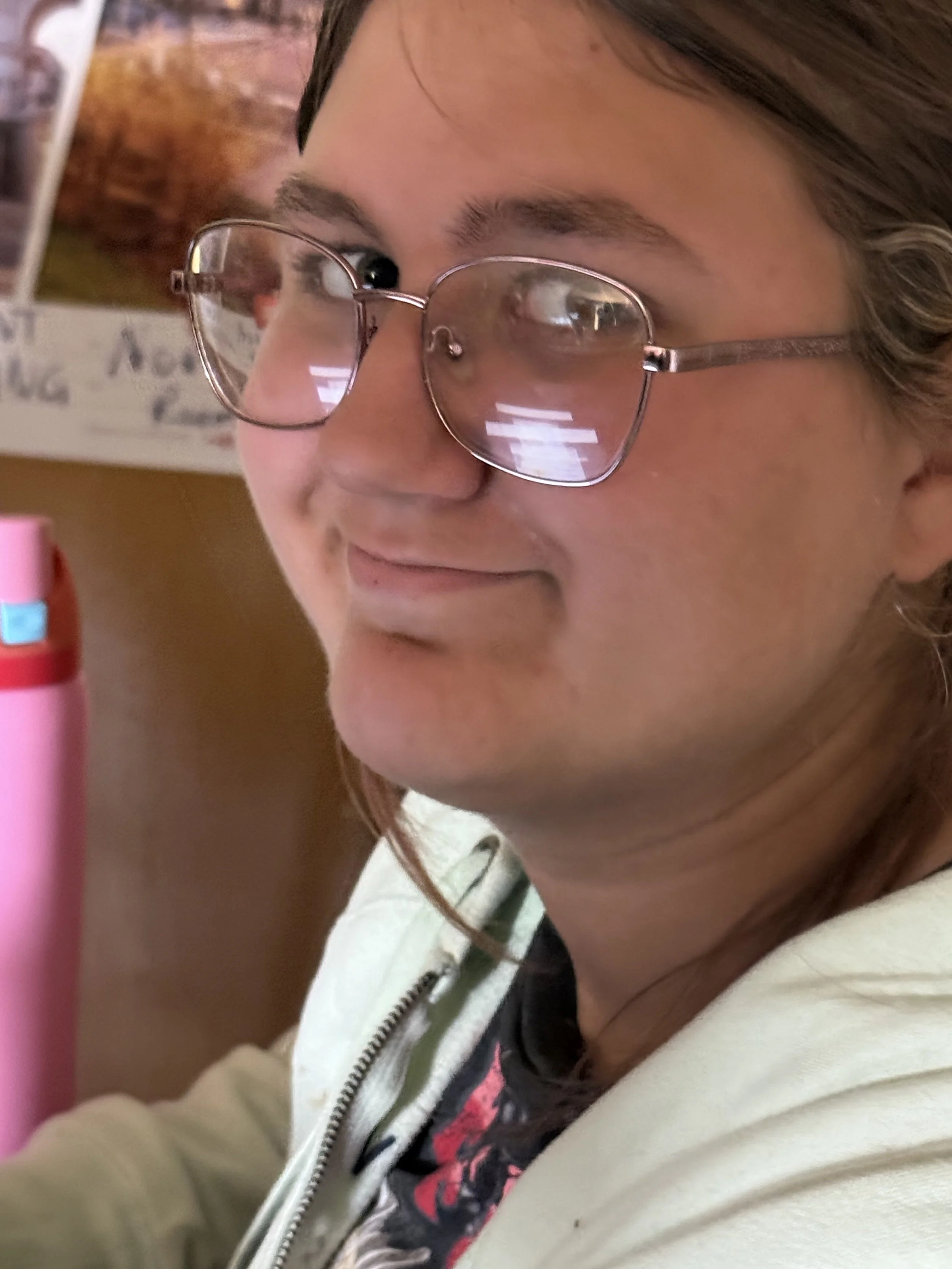 Close-up of a young woman wearing glasses, with a slight smile, in an indoor setting.