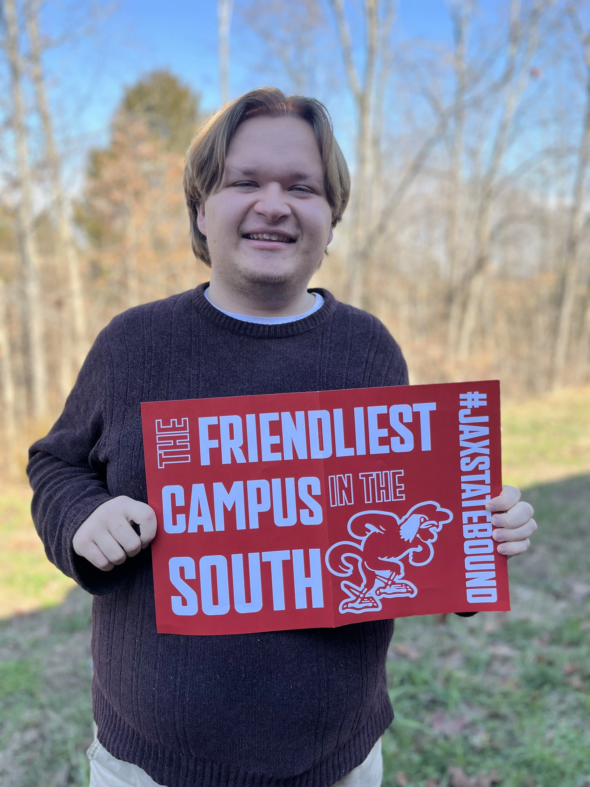 Young man with shoulder-length light brown hair smiling in front of a world map.