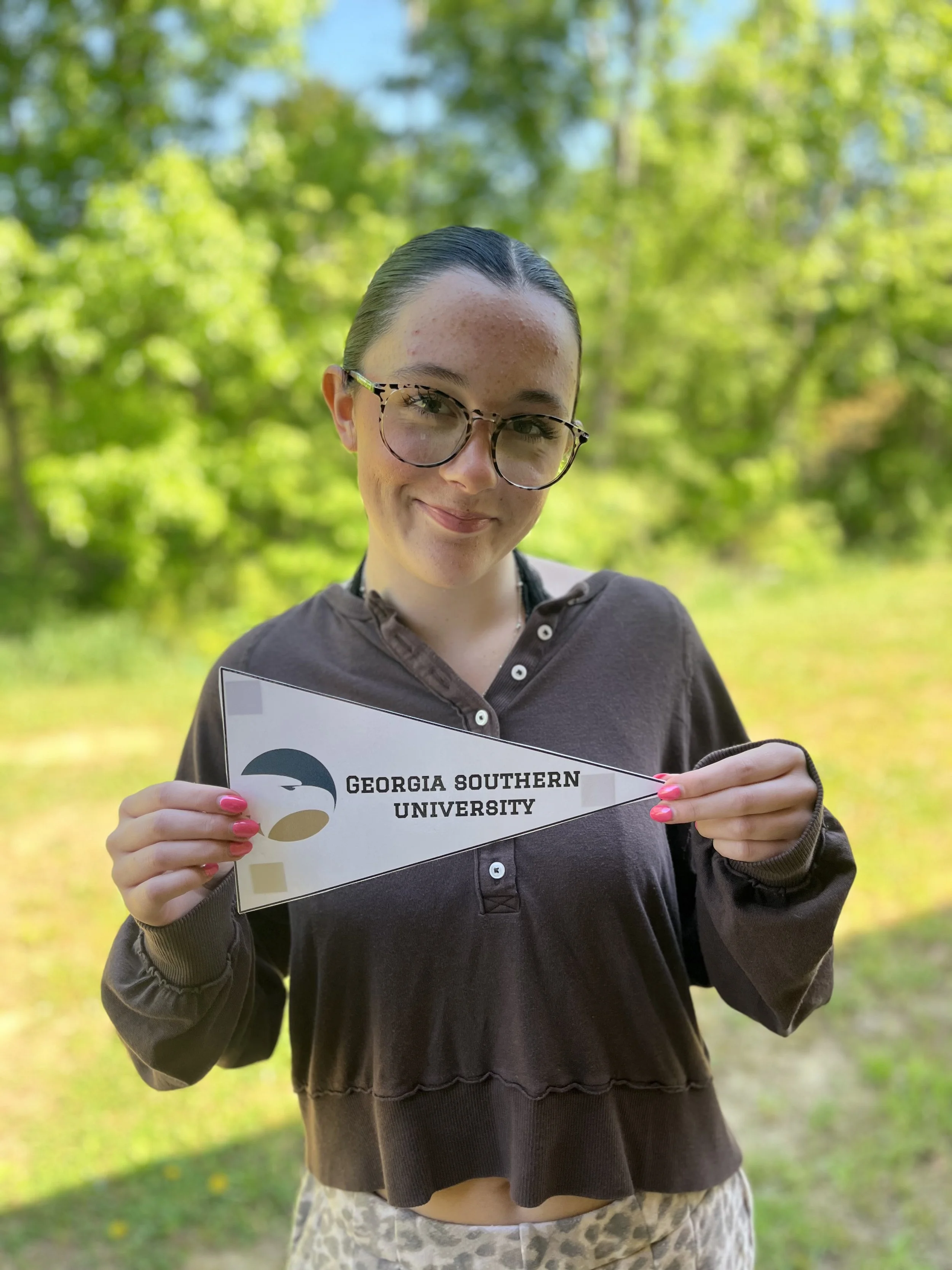 A young woman with long dark brown hair, fair skin, and freckles, smiling and looking at the camera.