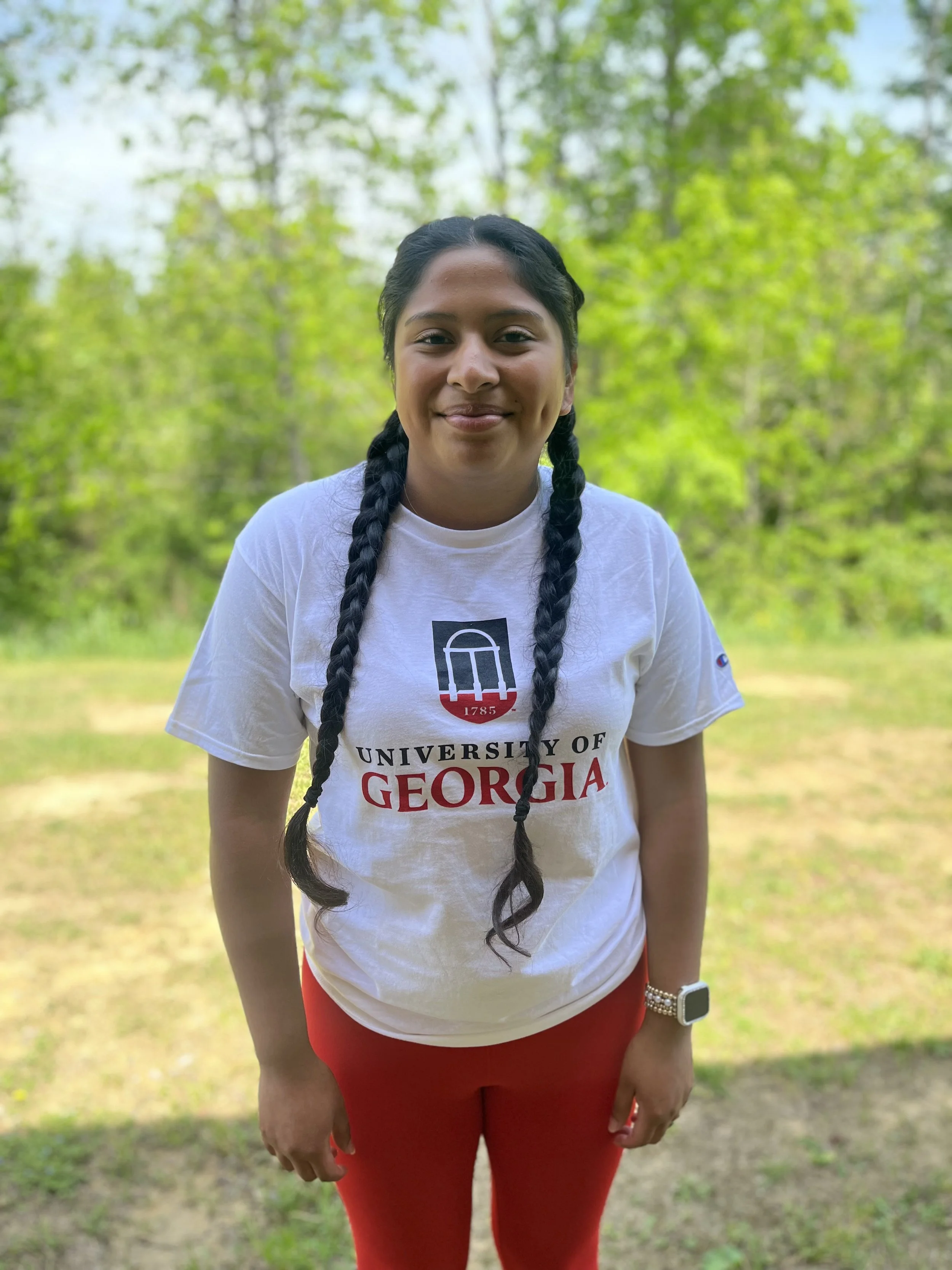 Close-up of a woman with dark hair, wearing earrings and a necklace with a cross pendant, smiling slightly, in an indoor setting.