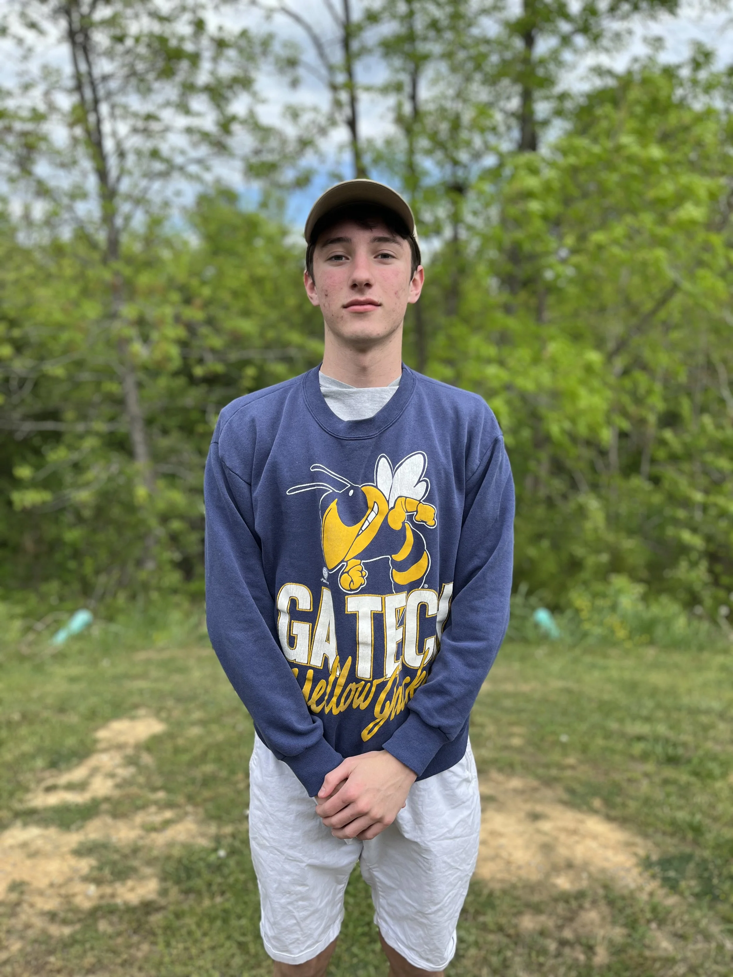 A teenage boy with short dark hair smiling, wearing a grey hoodie with a drawstring.