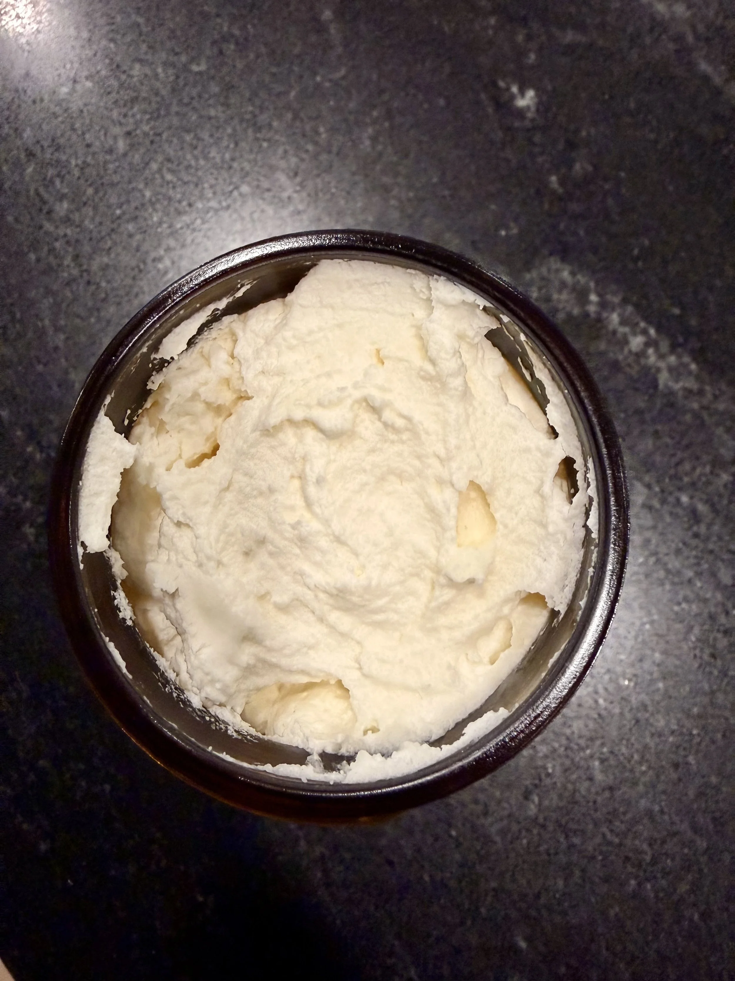 A container of vanilla ice cream viewed from above on a dark surface.