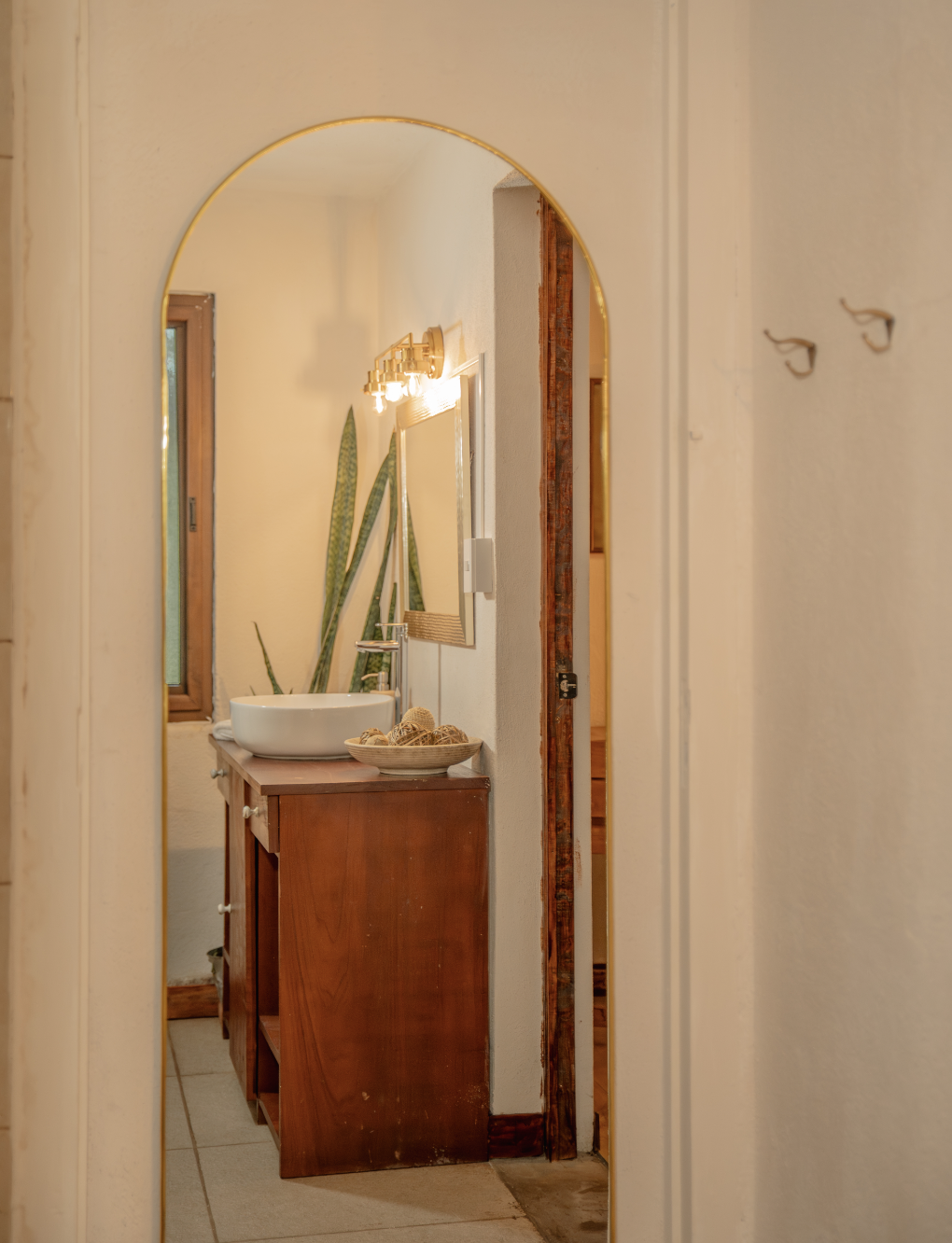 A bathroom vanity with a vessel sink, a mirror, and a light fixture, viewed through an arched doorway
