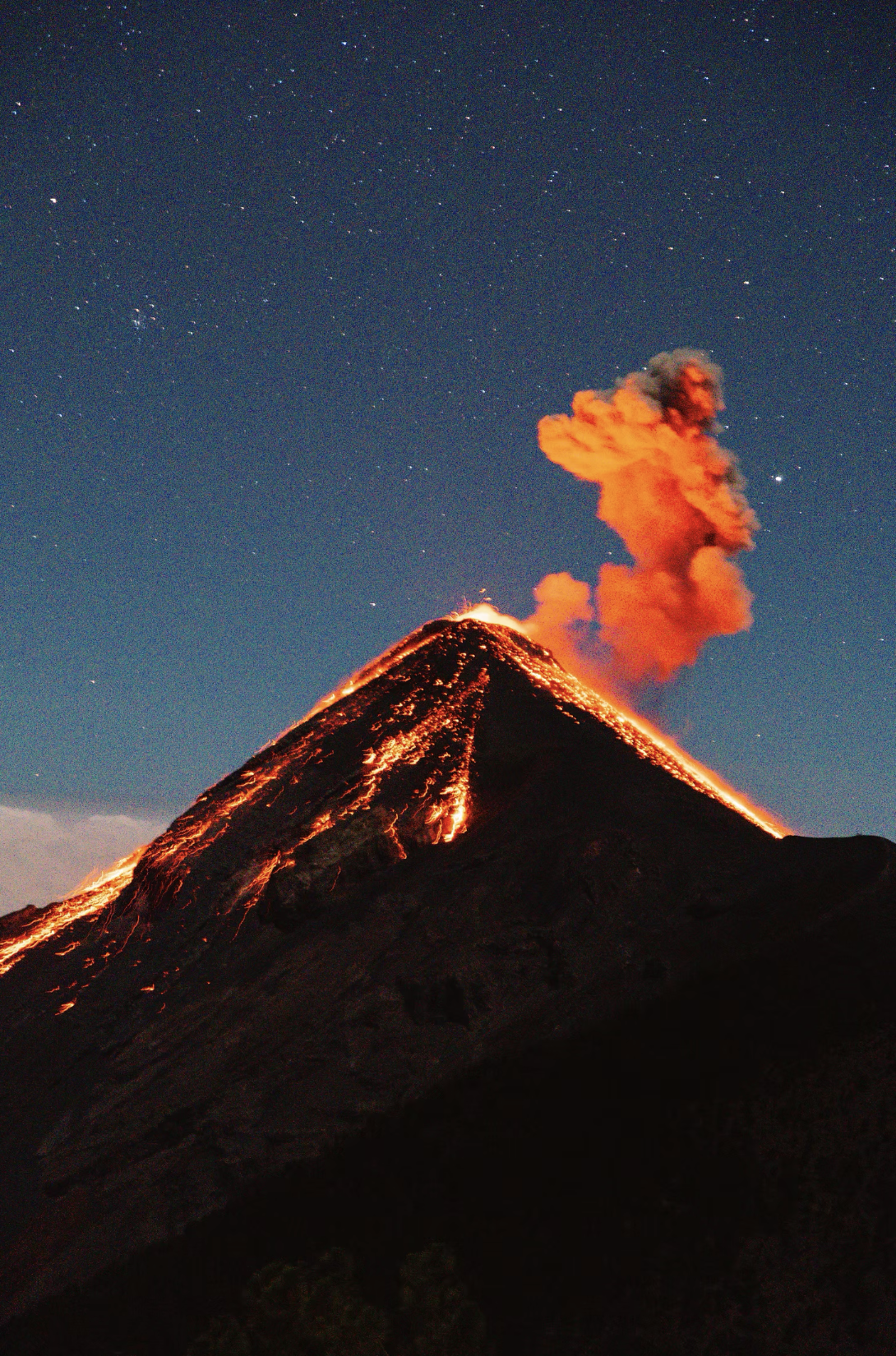 A volcano erupting at night, spewing orange lava and smoke into a star-filled sky.