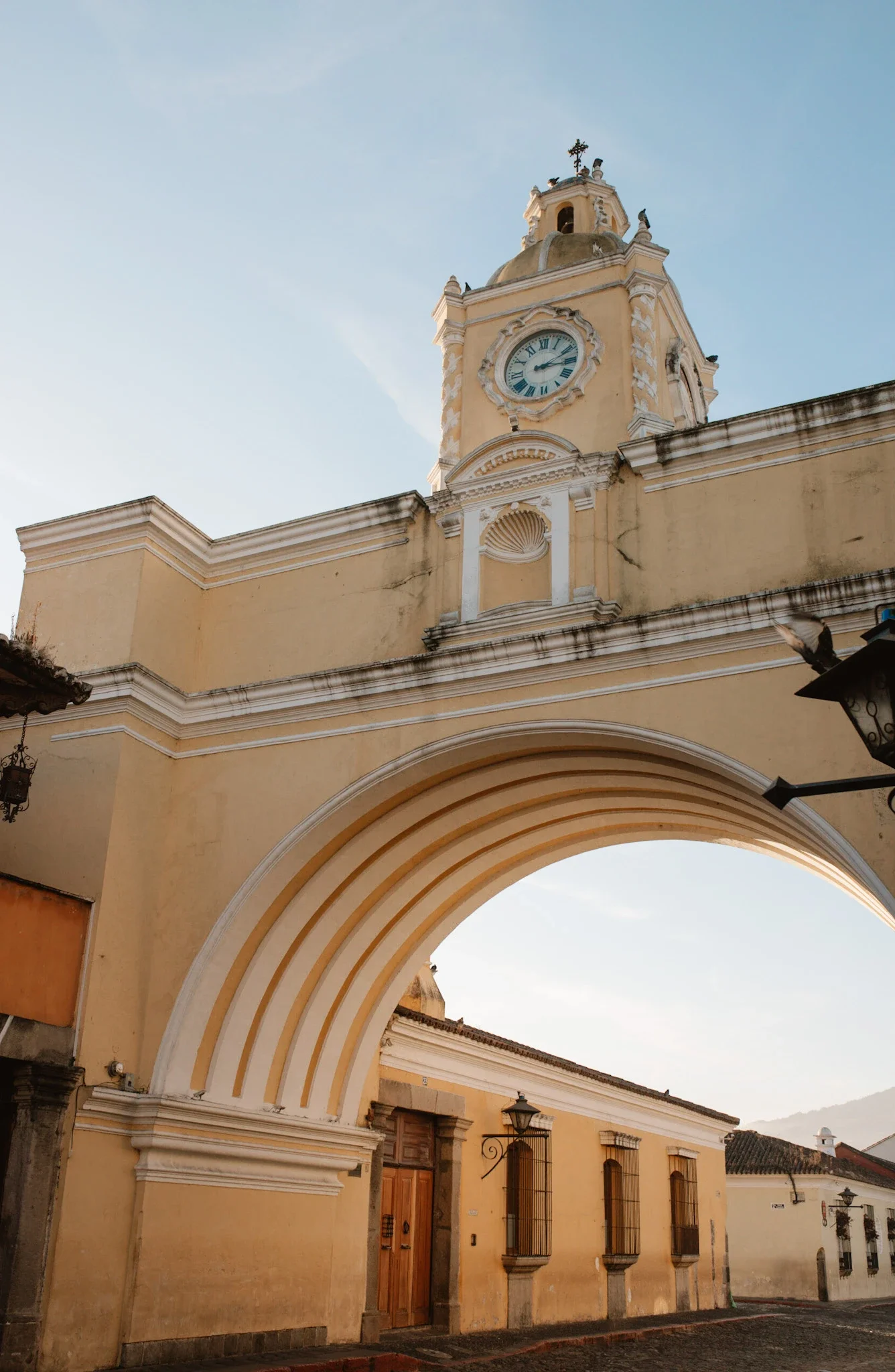 Historic yellow building with a clock tower and archway, located in a colonial-style town, under a clear sky.
