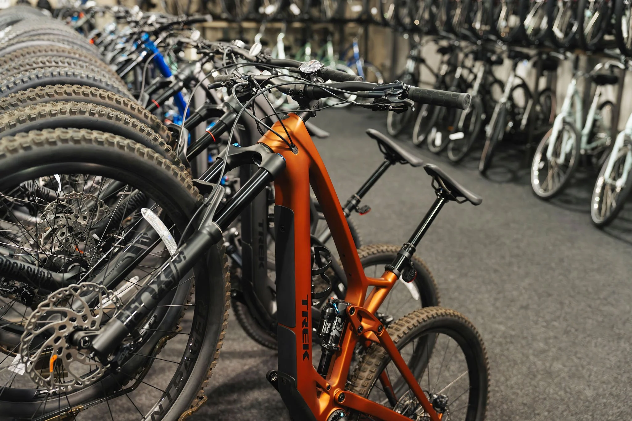 Orange mountain bike among other bikes with knobby tires inside a bike shop.