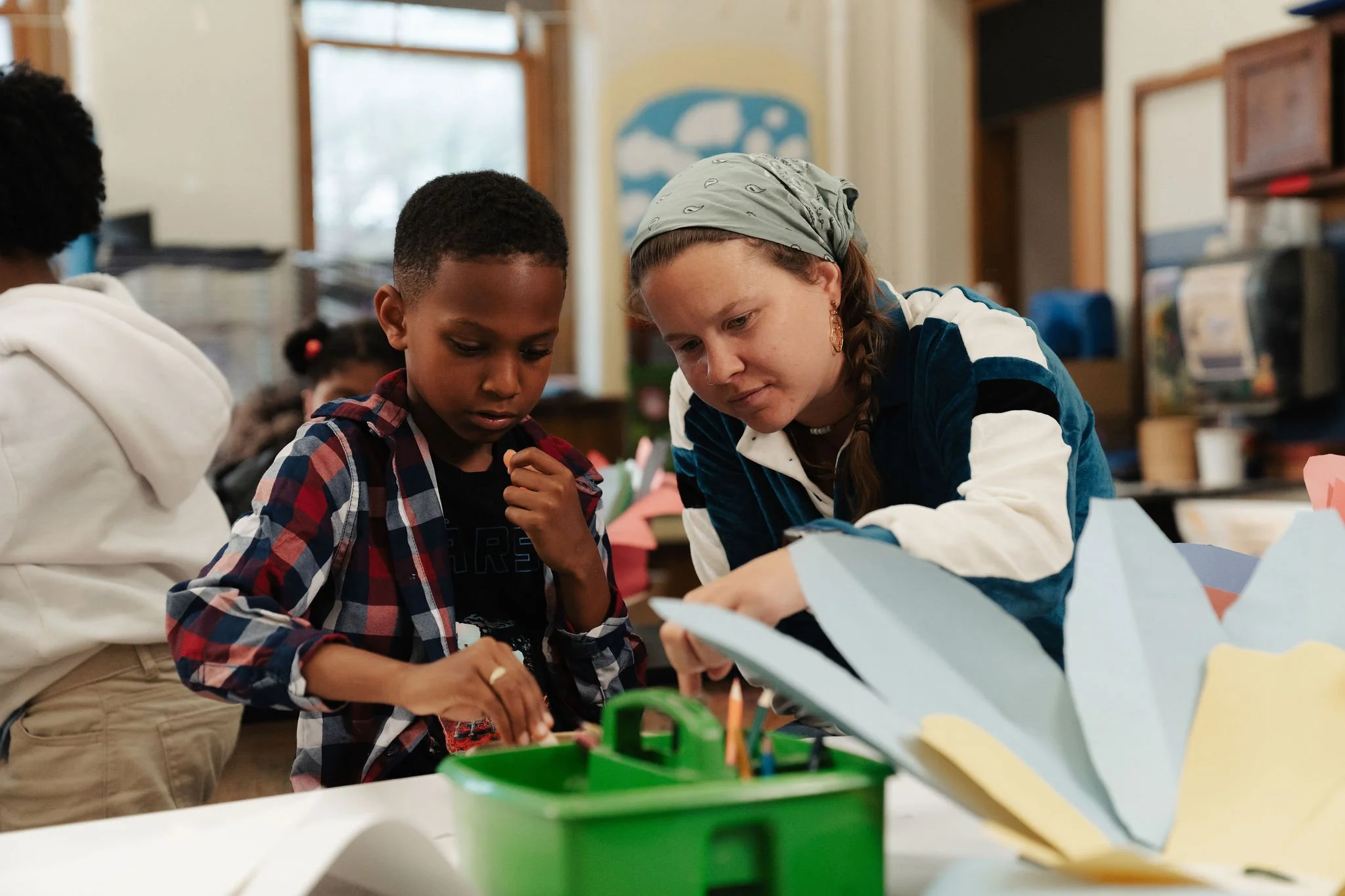 A woman and two children working together on a craft project at a table in a classroom.