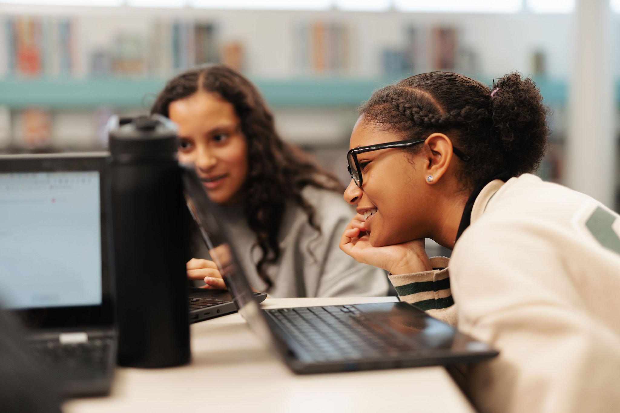 Two girls looking at a computer screen in a library or study room.