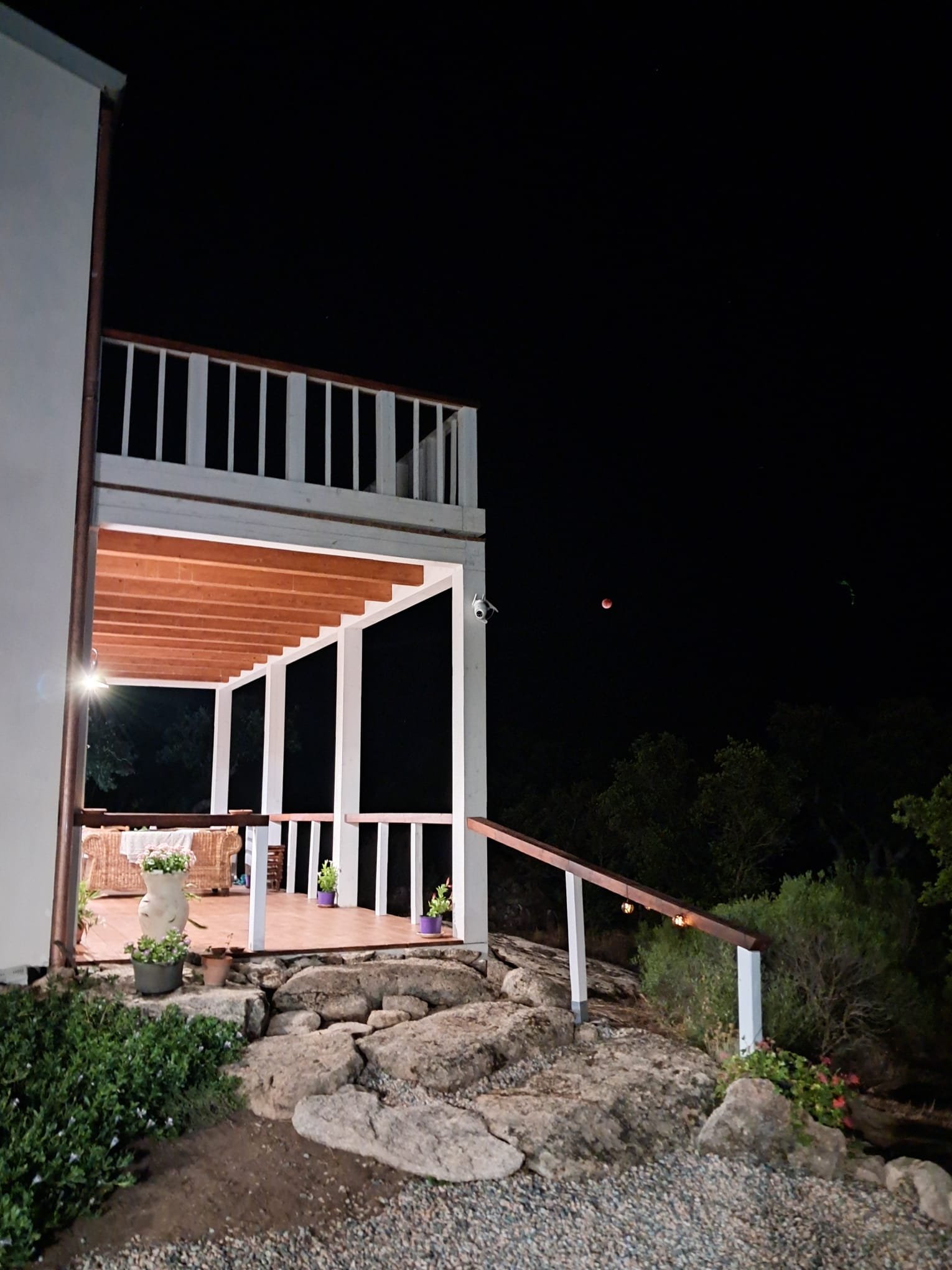 Veranda di una casa di notte con piante in vasi, illuminazione calda e vista su un cielo stellato