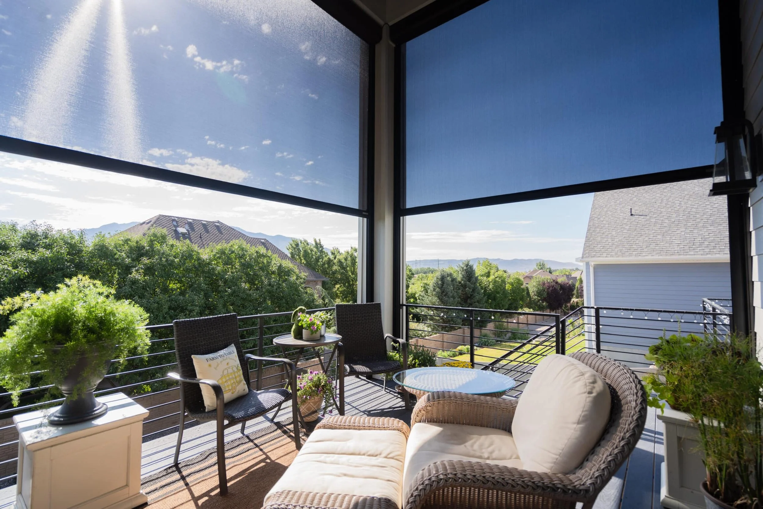 View of a screened-in porch with outdoor furniture, potted plants, and a scenic view of trees and houses in a suburban neighborhood.
