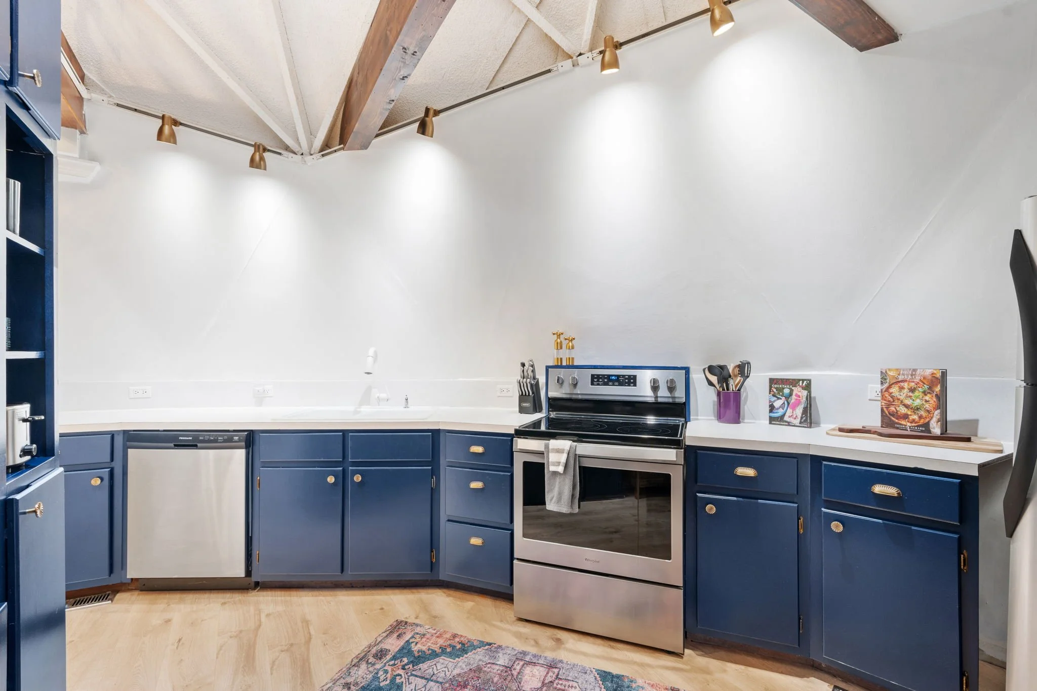 Modern kitchen with wooden cabinets. Contains a small sink, a beverage refrigerator, a coffee maker, and a light-colored rug on the floor.