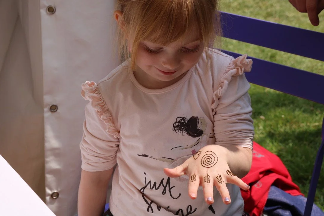 A young girl with red hair looking at her hand, which has intricate henna-style designs including spiral and leaf patterns.