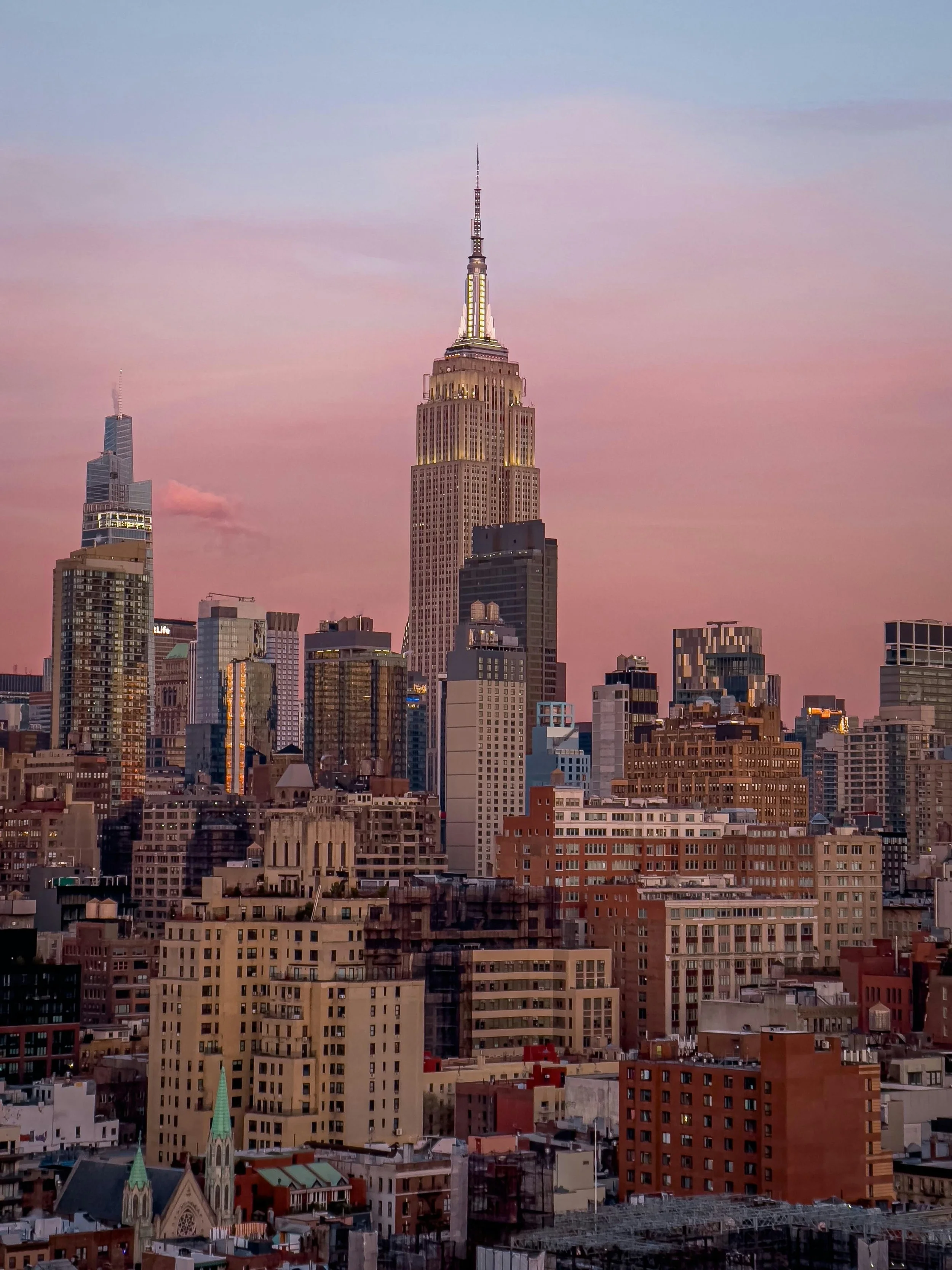 Sunset view of the New York City skyline featuring the Empire State Building illuminated against a pink and blue sky.