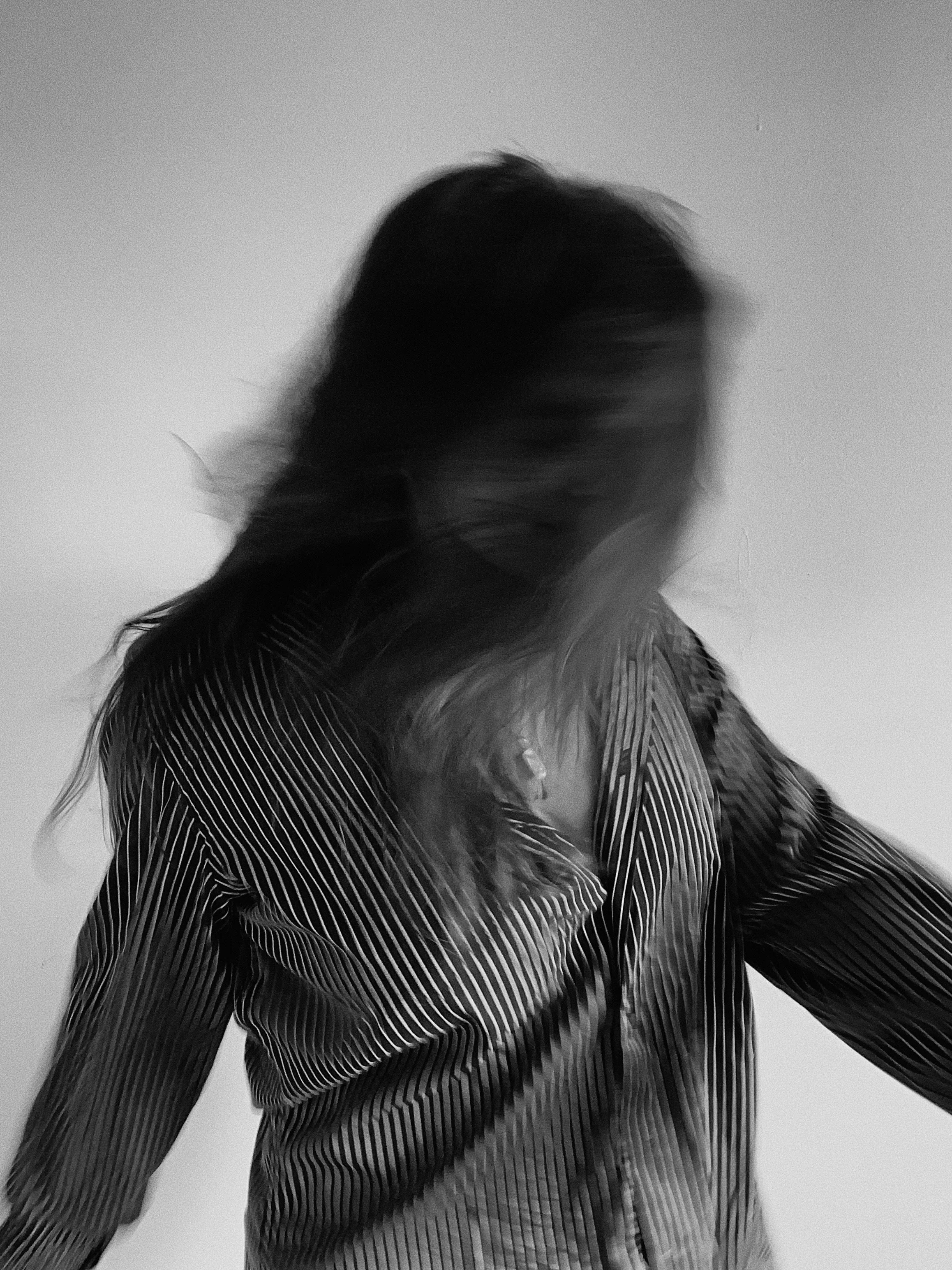 A blurred black and white photo of a woman with long hair, wearing a striped shirt, moving or turning quickly.
