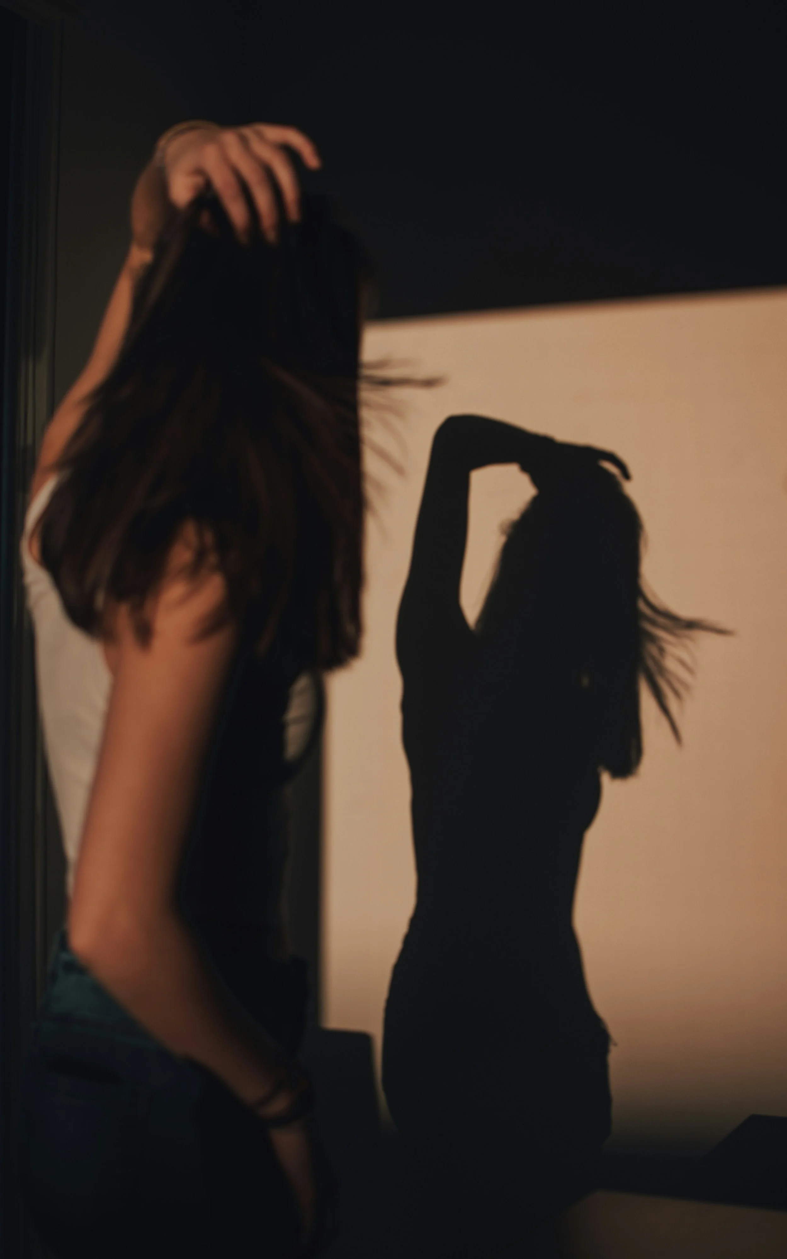 A woman standing in front of a screen, creating a shadow silhouette with her arm raised and head tilted slightly, with her long hair flowing.
