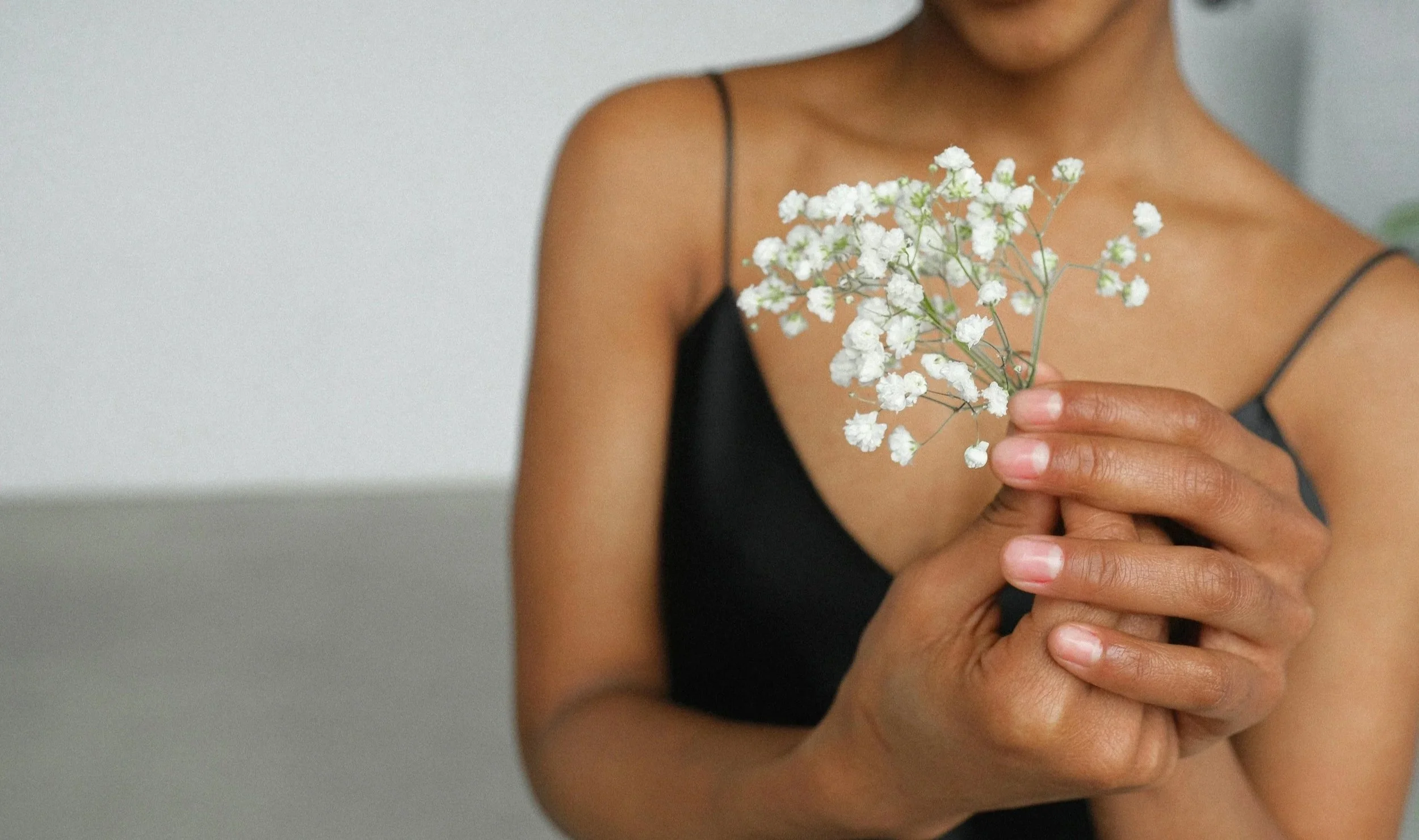 A woman in a black spaghetti strap top holding a small bouquet of white baby's breath flowers.