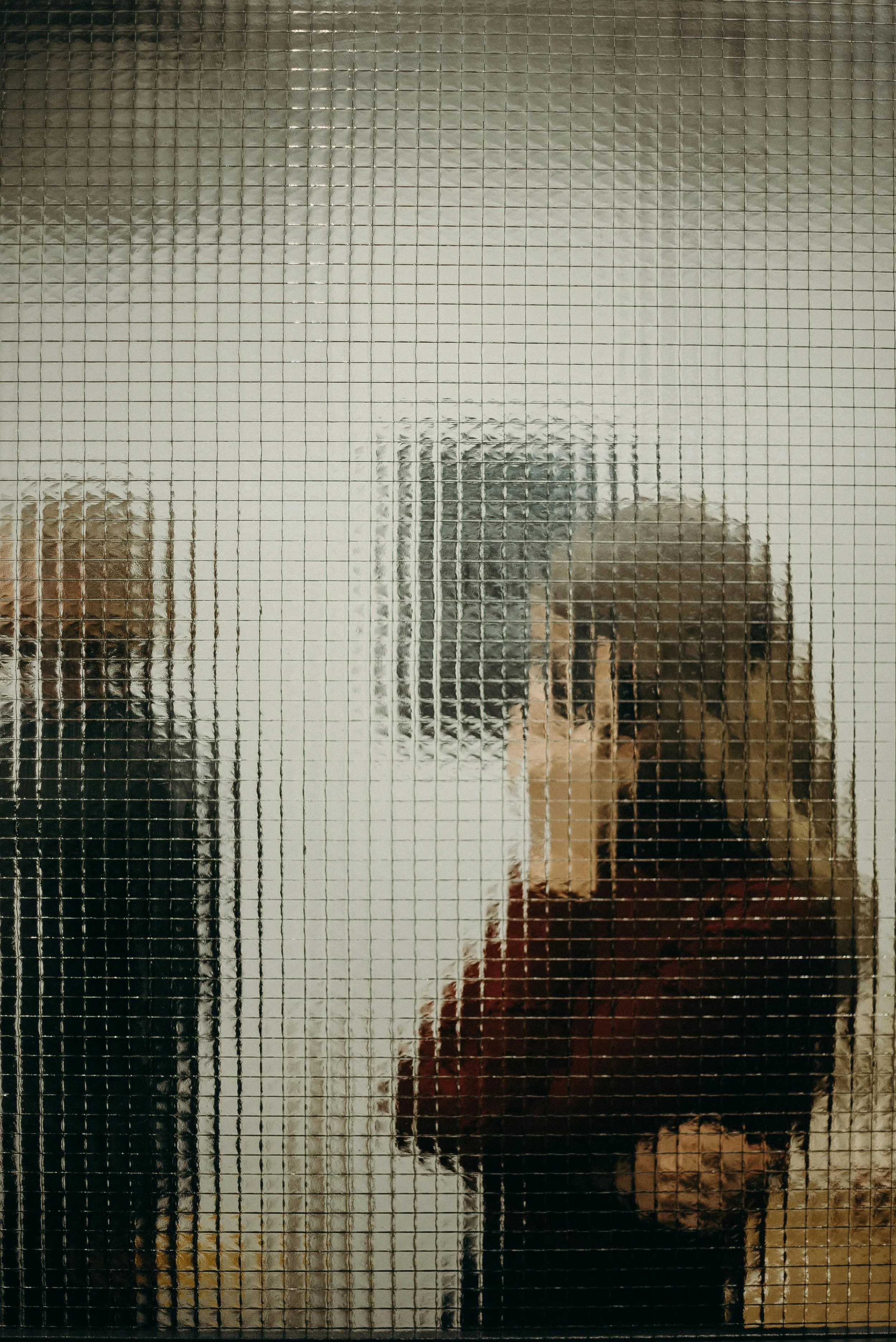 Person taking a mirror selfie with a smartphone, seen through a textured glass door.
