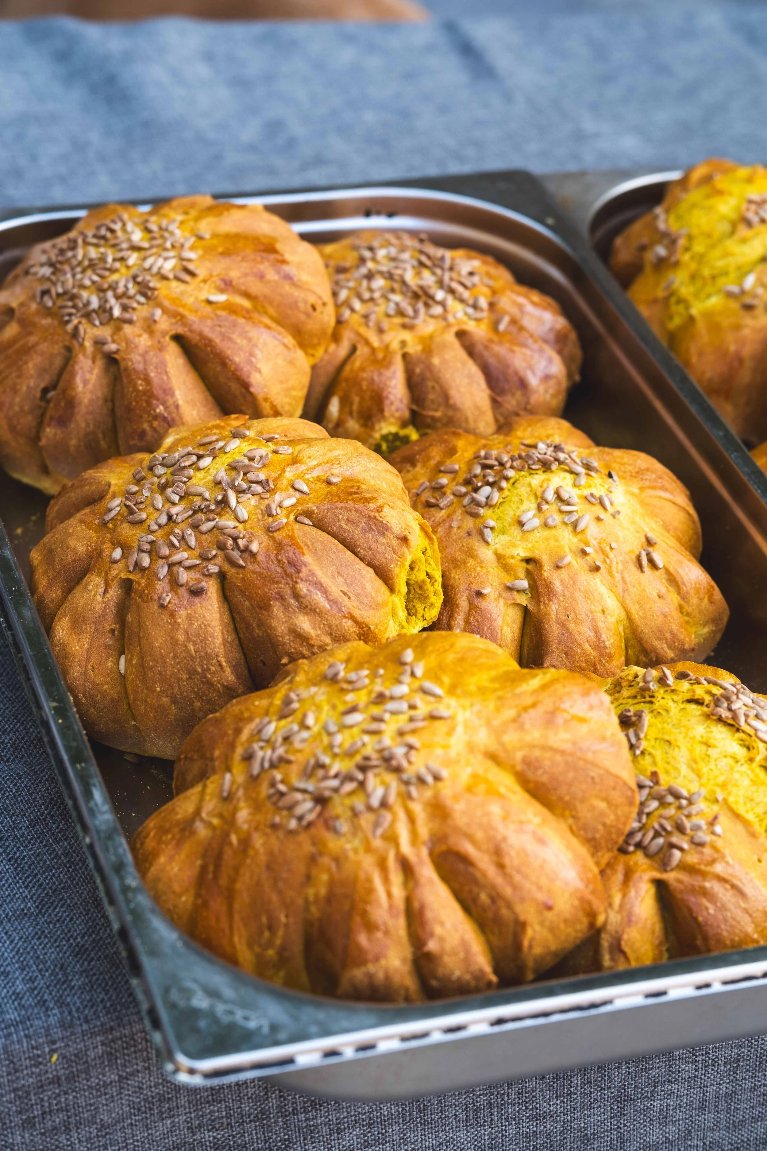 Fresh baked pumpkin-shaped bread rolls topped with sunflower seeds in a metal baking pan.