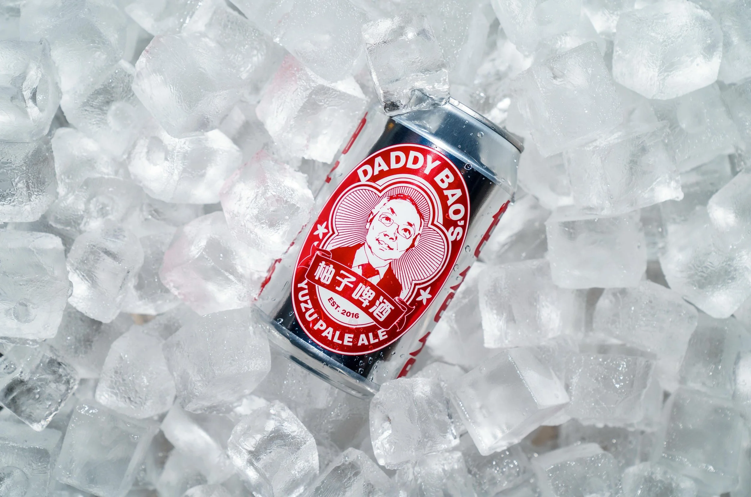 A can of Daddy Bao's Zhu Zuzhu Pale Ale resting on ice cubes, with a red and black label featuring a portrait of a man wearing glasses.