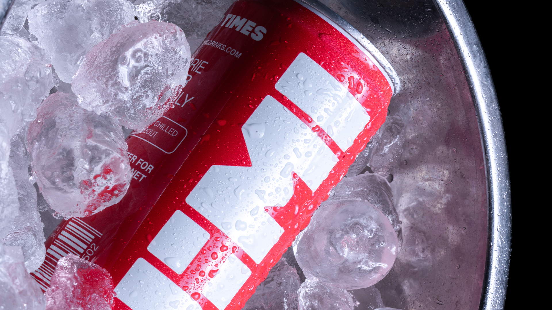 A red and white can of soft drink resting on ice cubes in a metal container, with water droplets on the can.