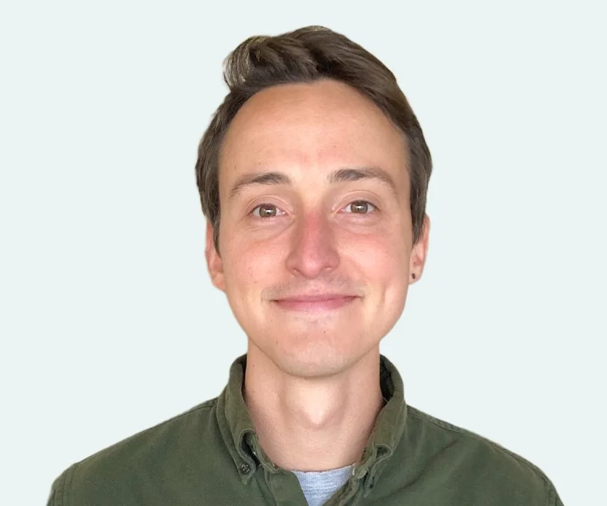 A young man with short brown hair, light skin, and a slight smile, wearing a dark green button-up shirt, standing against a plain light background.