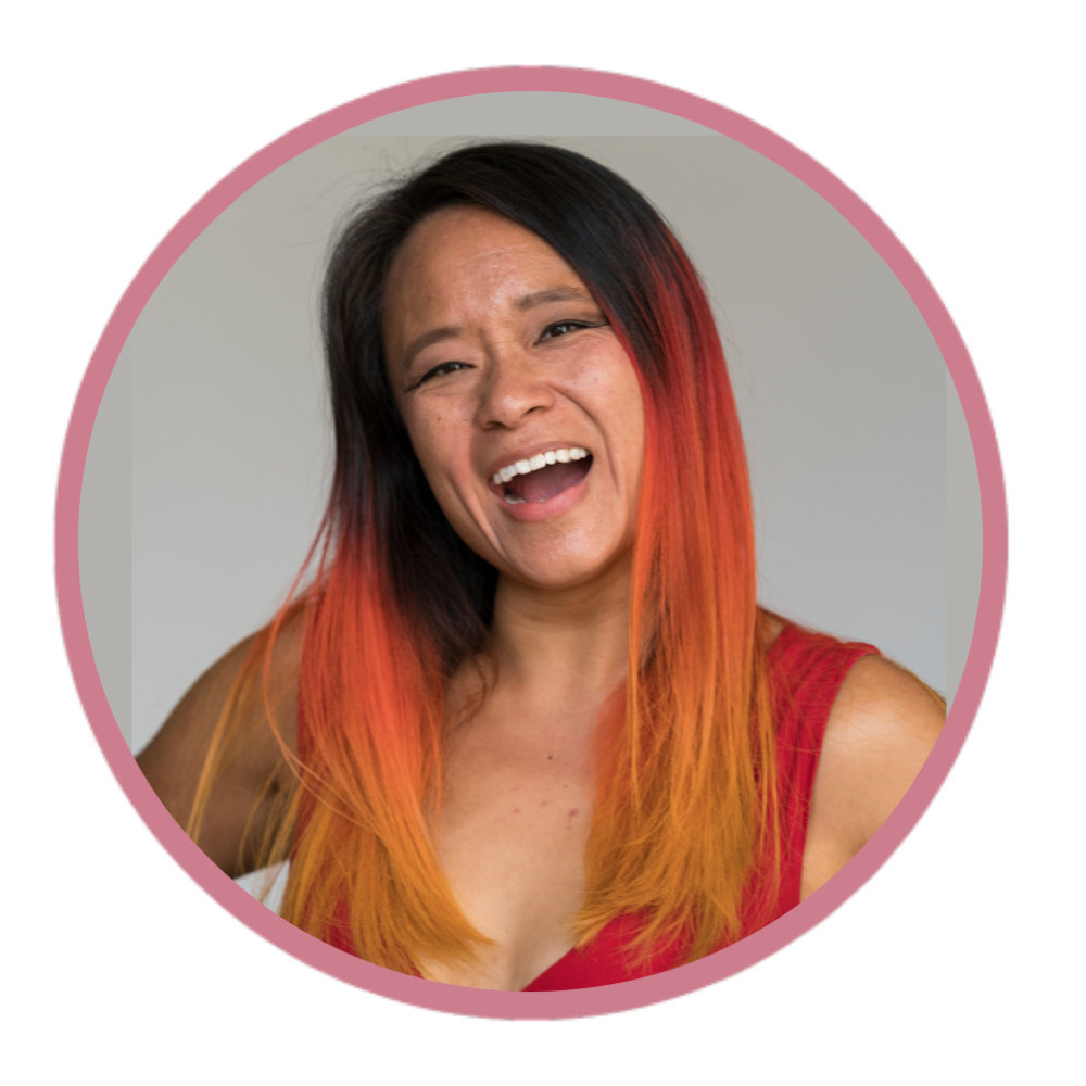 A woman with multicolored hair, black with red and orange ends, smiling with her mouth open, wearing a red sleeveless top.