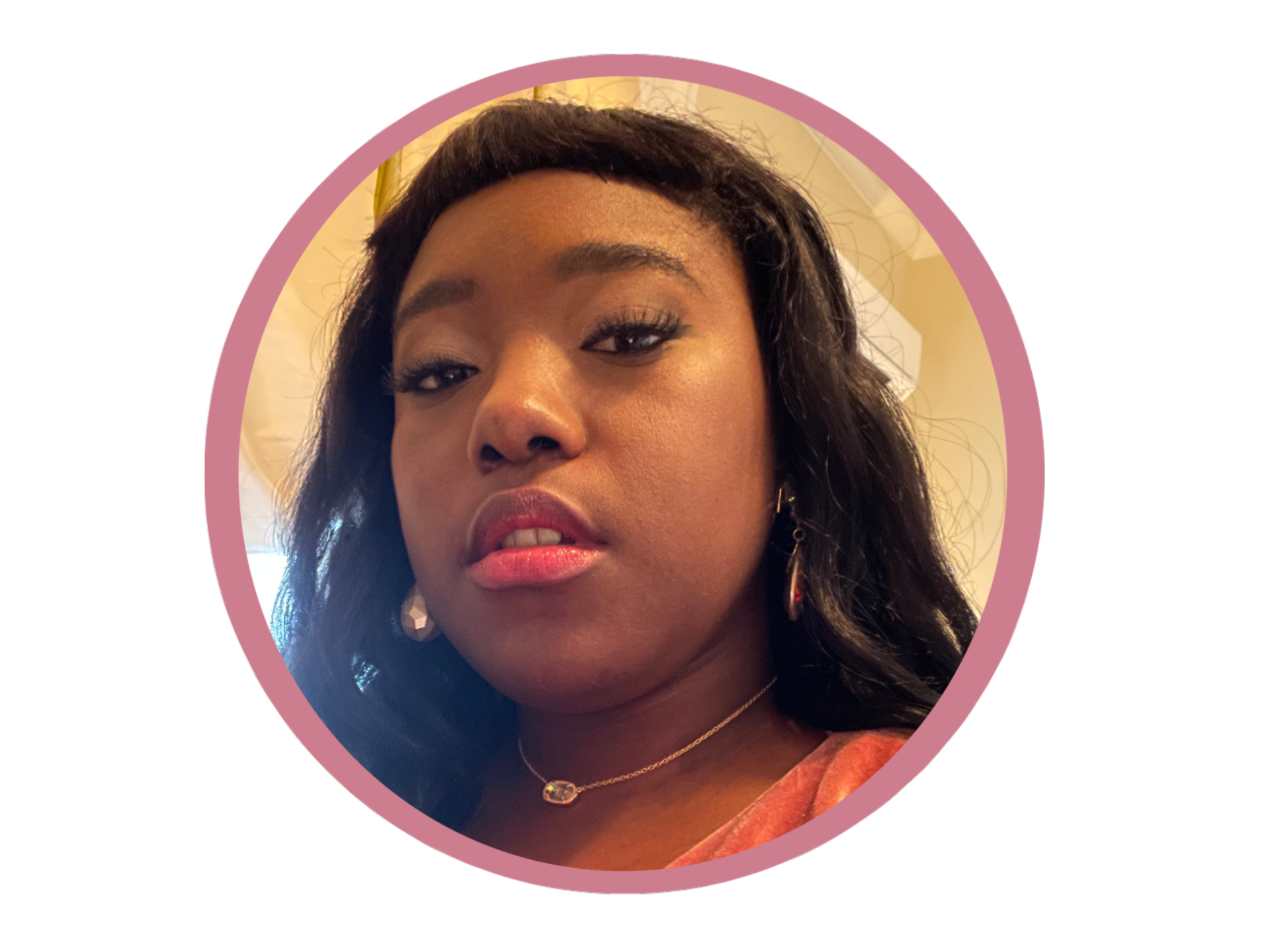 Close-up of a woman with dark hair, gold earrings, a delicate necklace, and makeup, looking at the camera.