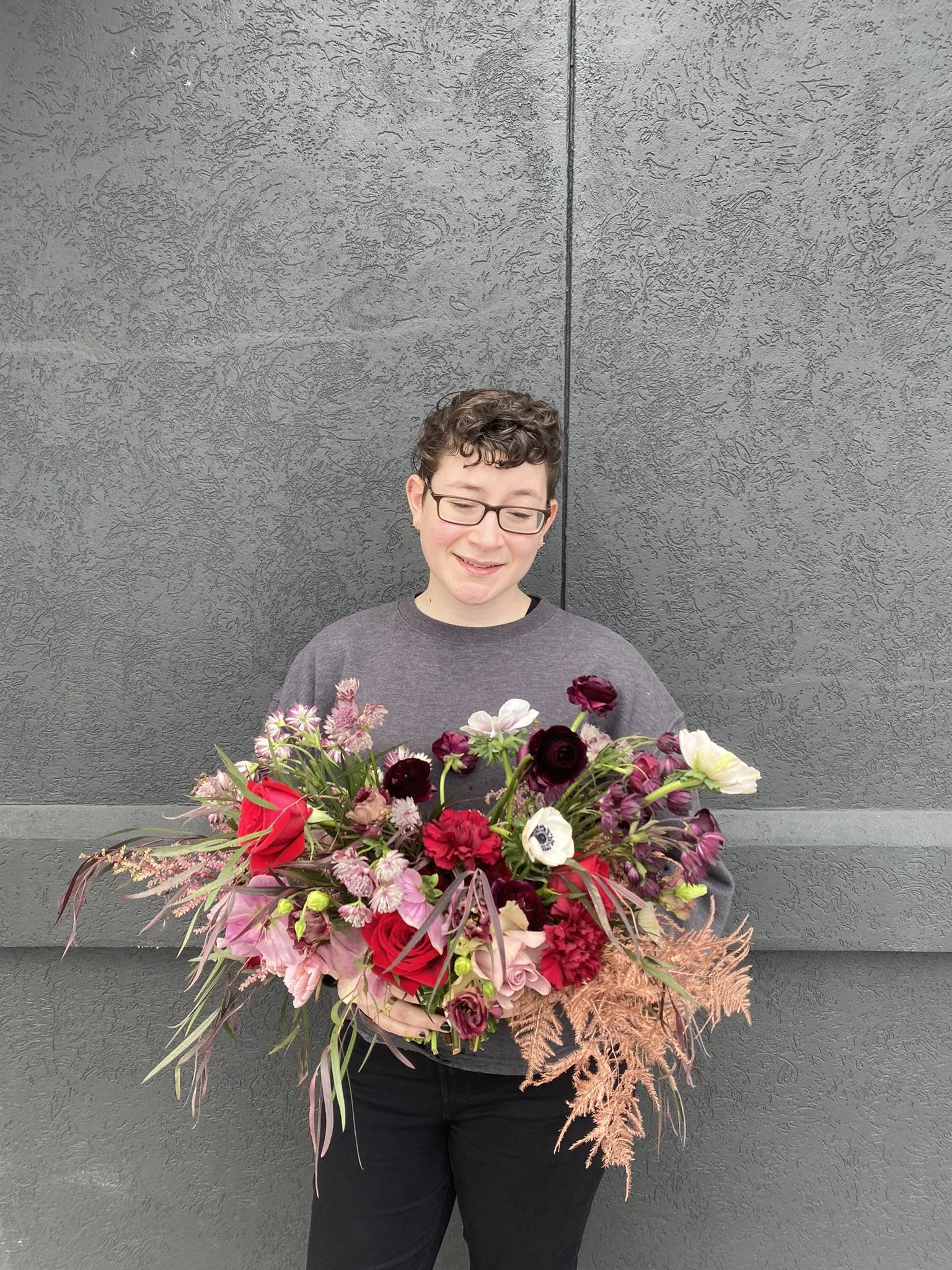 Person with short curly hair and glasses holding a large bouquet of colourful flowers