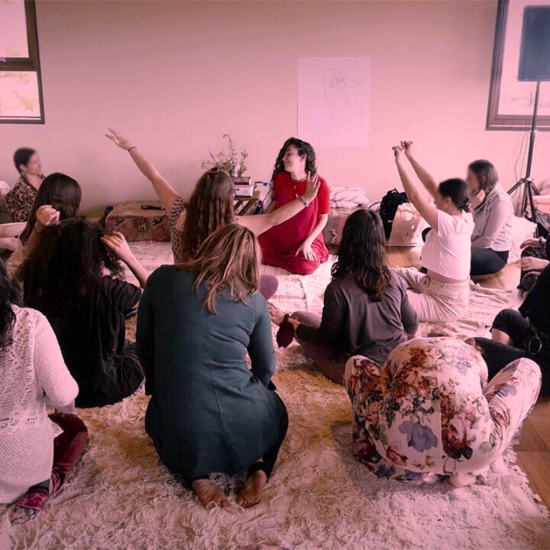Group of women seated in a circle during a workshop, one woman in red at the centre