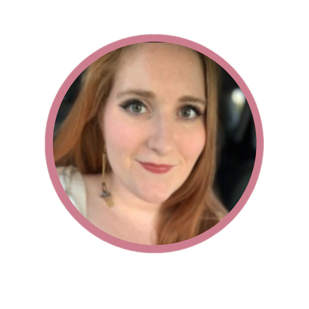 Close-up photo of a woman with red hair and blue eyes, smiling, wearing makeup and earrings, with a blurred background.