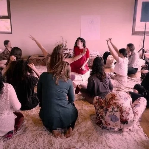 Group of women seated in a circle during a workshop, one woman in red at the centre representing online courses for self development