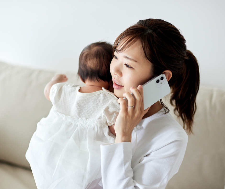 A woman holding a baby while talking on her cell phone in a bright room.