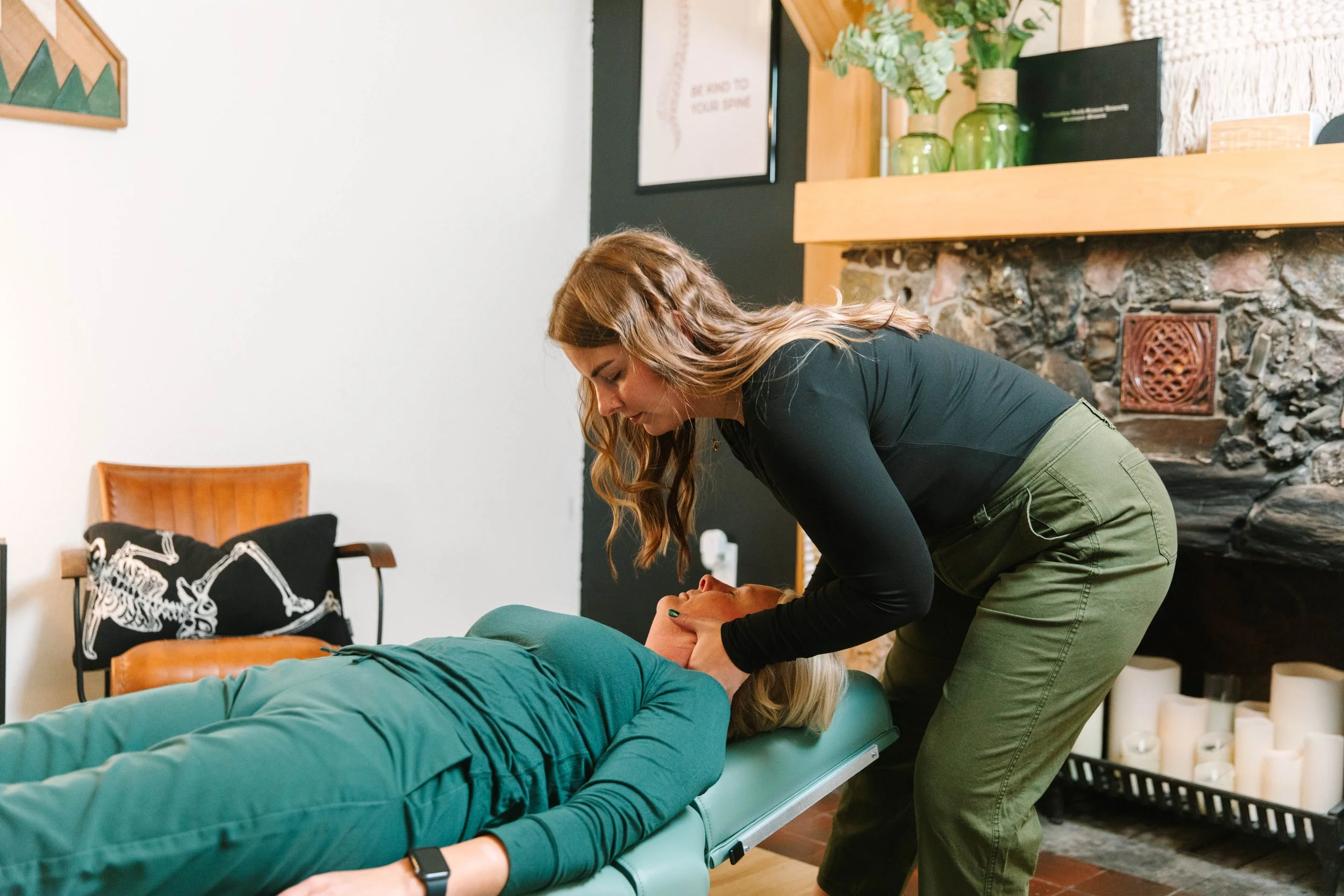 A person receiving a chiropractic adjustment or massage while lying face down on a treatment table, with another person applying pressure to their back.