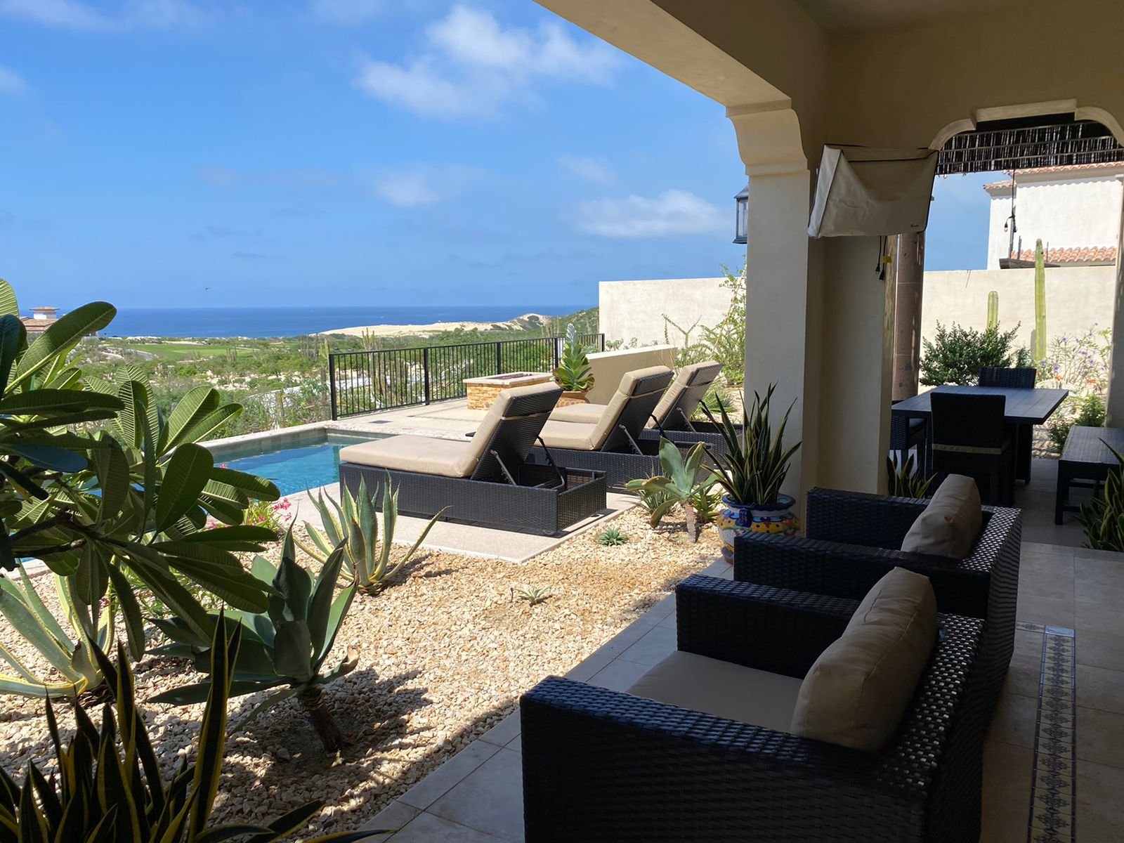 Outdoor patio with cushioned chairs, a small pool, and a scenic view of a landscape and ocean in the distance.