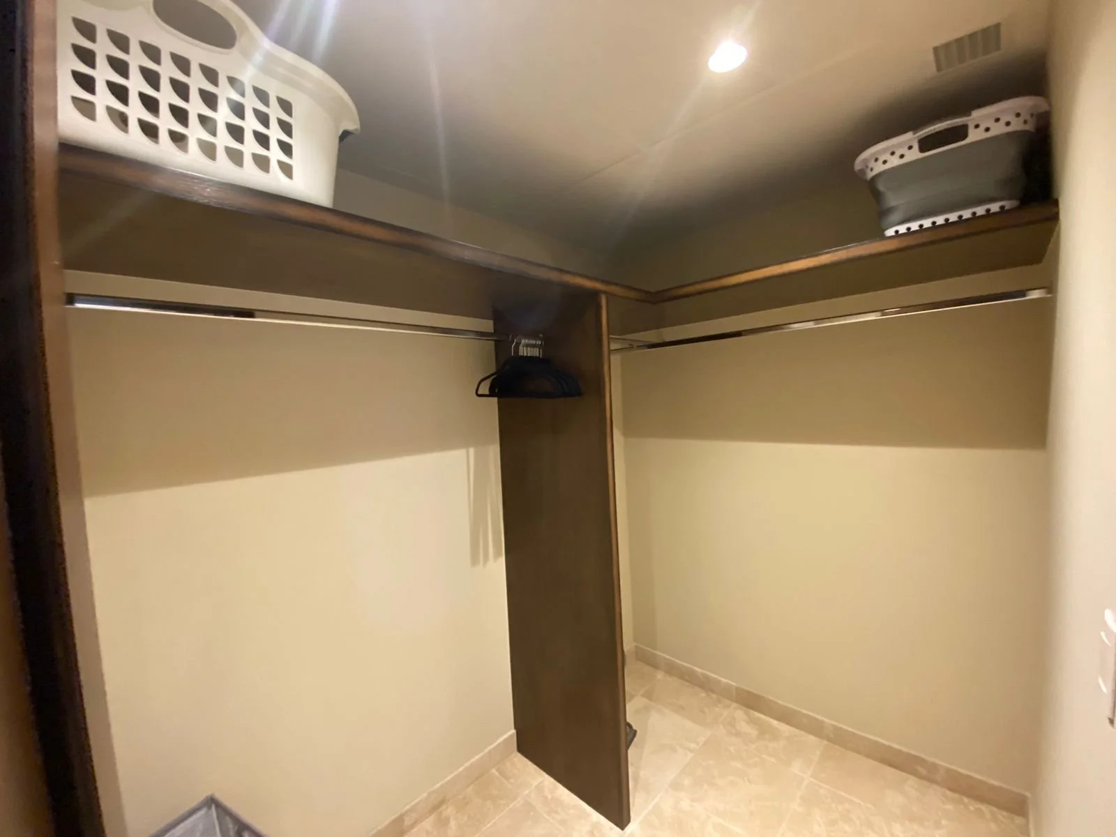 Empty walk-in closet with two shelves at the top, a hanging rod with a few hangers, and various storage baskets and containers on the shelves.