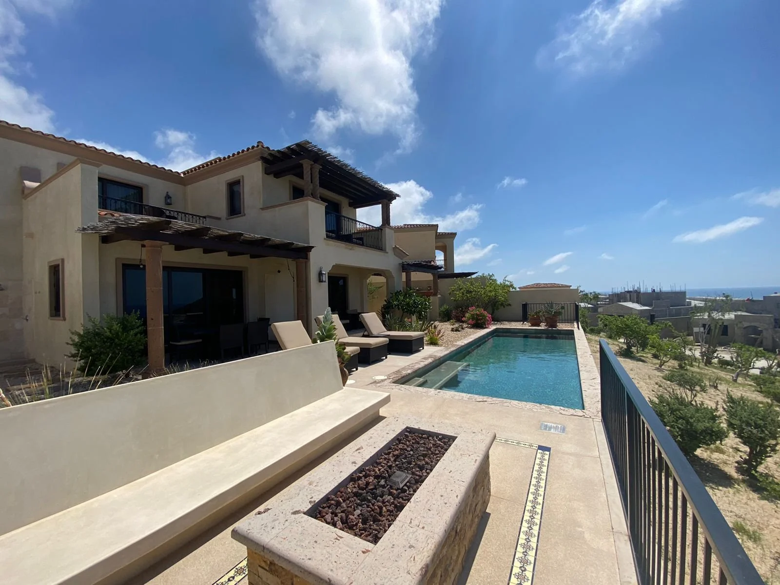 Luxury house with a swimming pool, lounge chairs, and a outdoor seating area under a blue sky with clouds in a coastal setting.