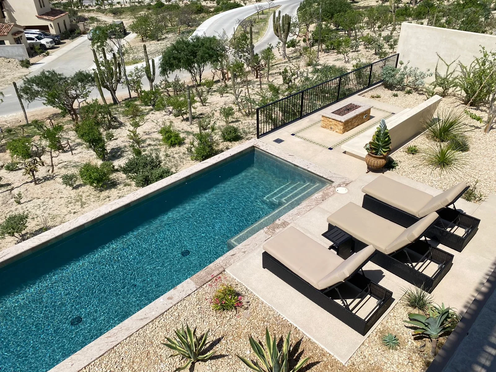 A backyard hot tub with surrounding sun loungers and desert landscaping, including cacti and succulents, overlooking a desert landscape with trees and a winding road.