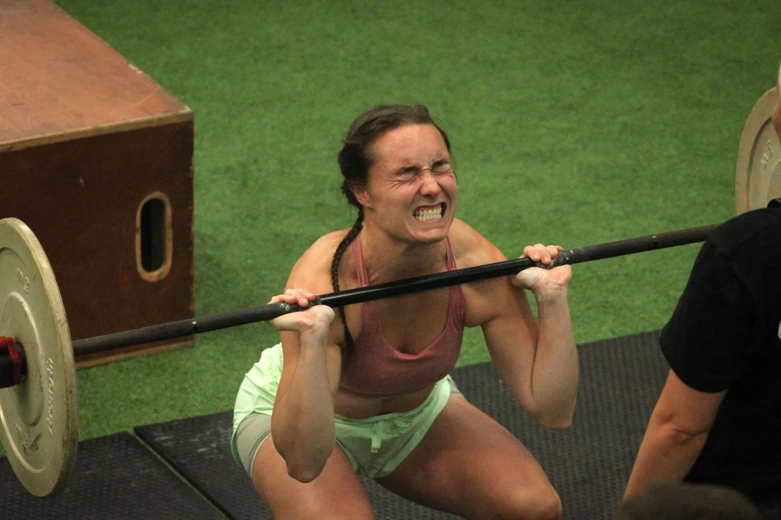 Woman lifting a barbell with weights at gym, showing a strained facial expression.