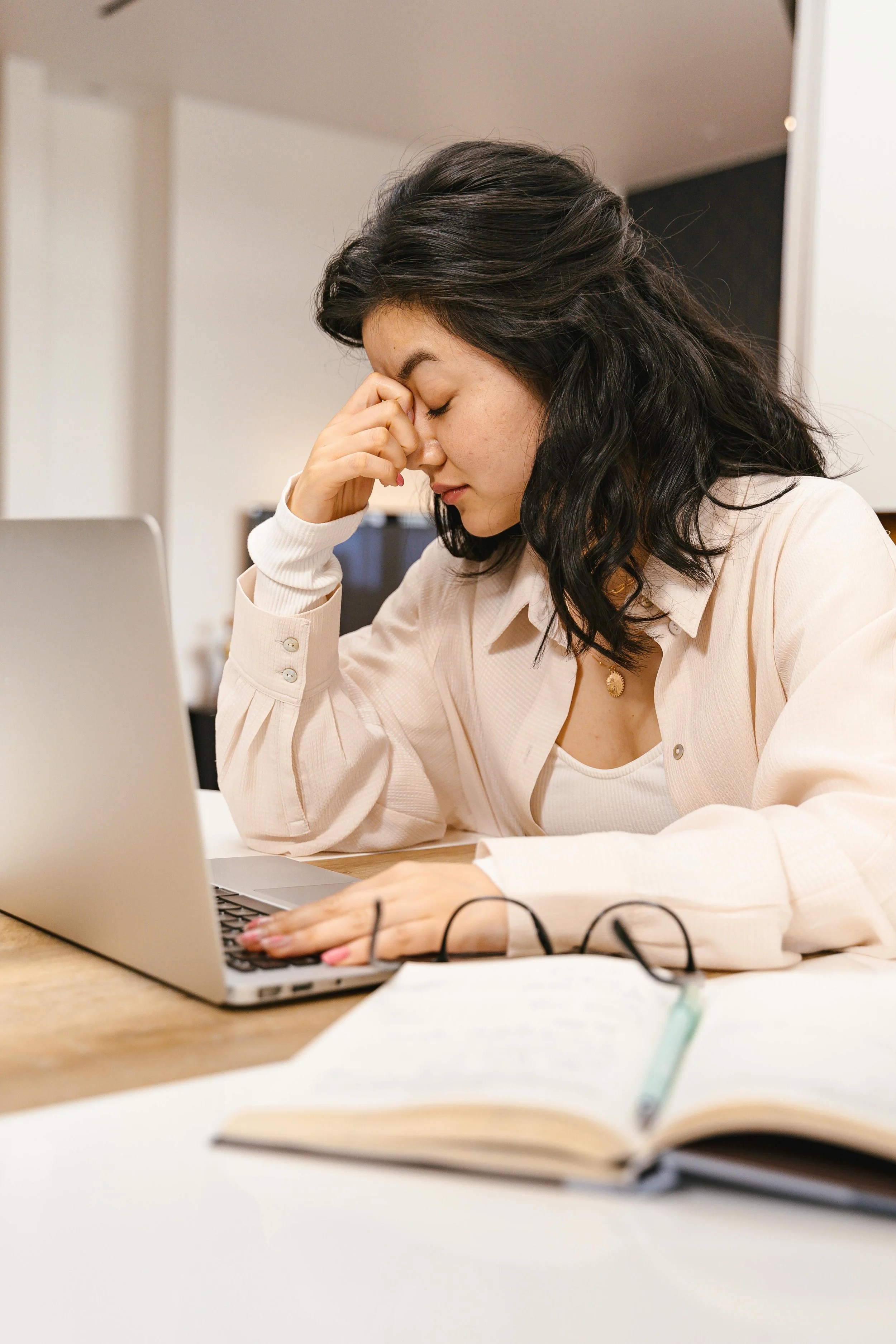 Professional woman at desk with head bowed and eyes closed showing signs of burnout and chronic stress, representing anxiety therapy in New York