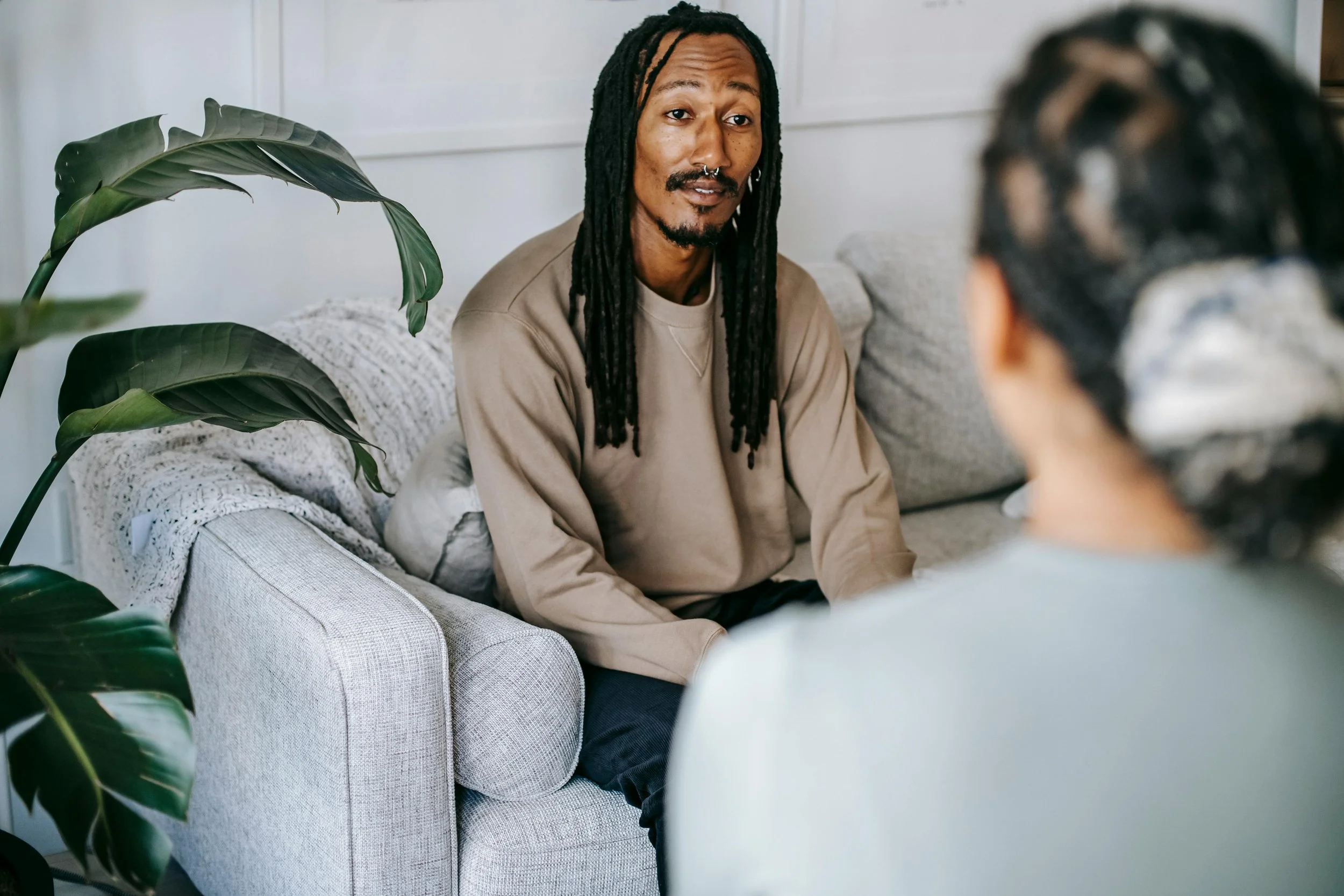 A man sitting on a couch, talking with a therapist in a calm, light-filled space — representing openness, trust, and the beginning of healing.
