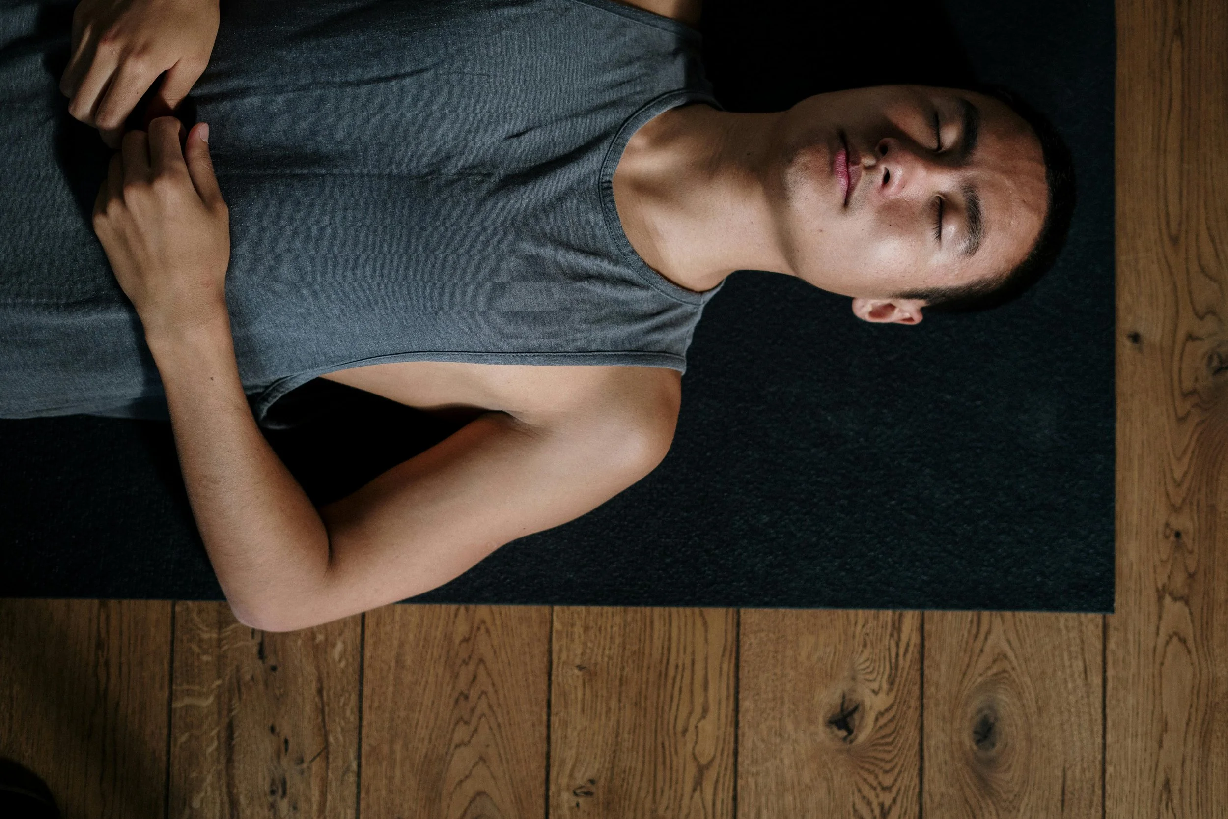 Man lying on a yoga mat with eyes closed, practicing rest and nervous system regulation in trauma therapy.