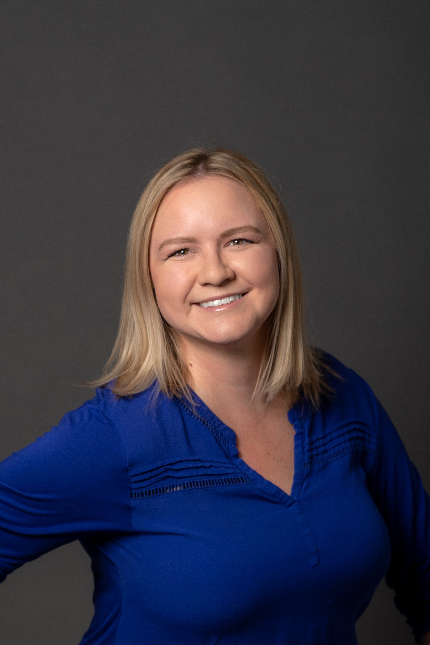 Image of person identifying as a woman with blond hair, brown eyes. Wearing a blue shirt