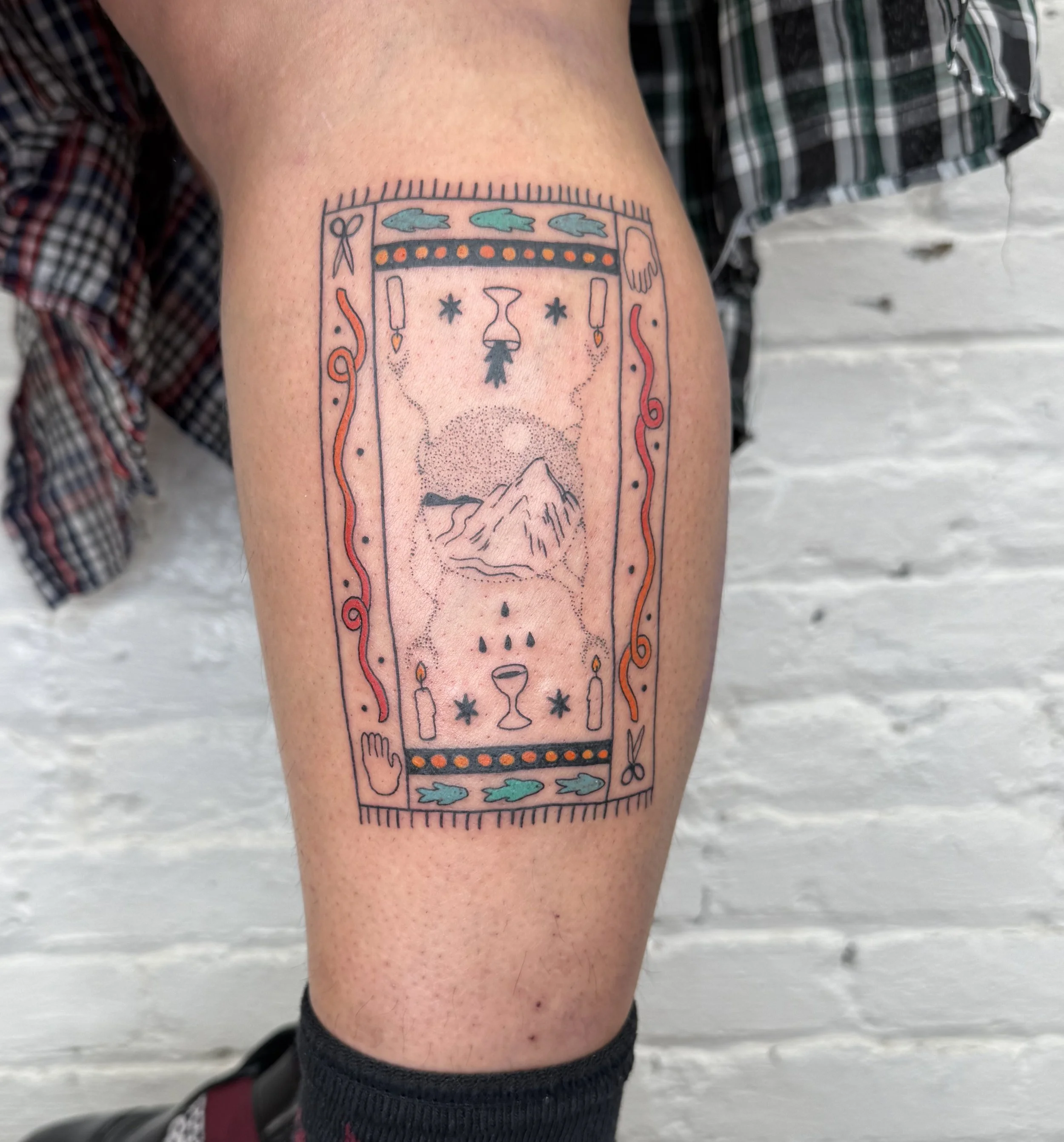 Tattoo of a decorative framed design featuring mountains, a starry sky, candles, and various symbols.