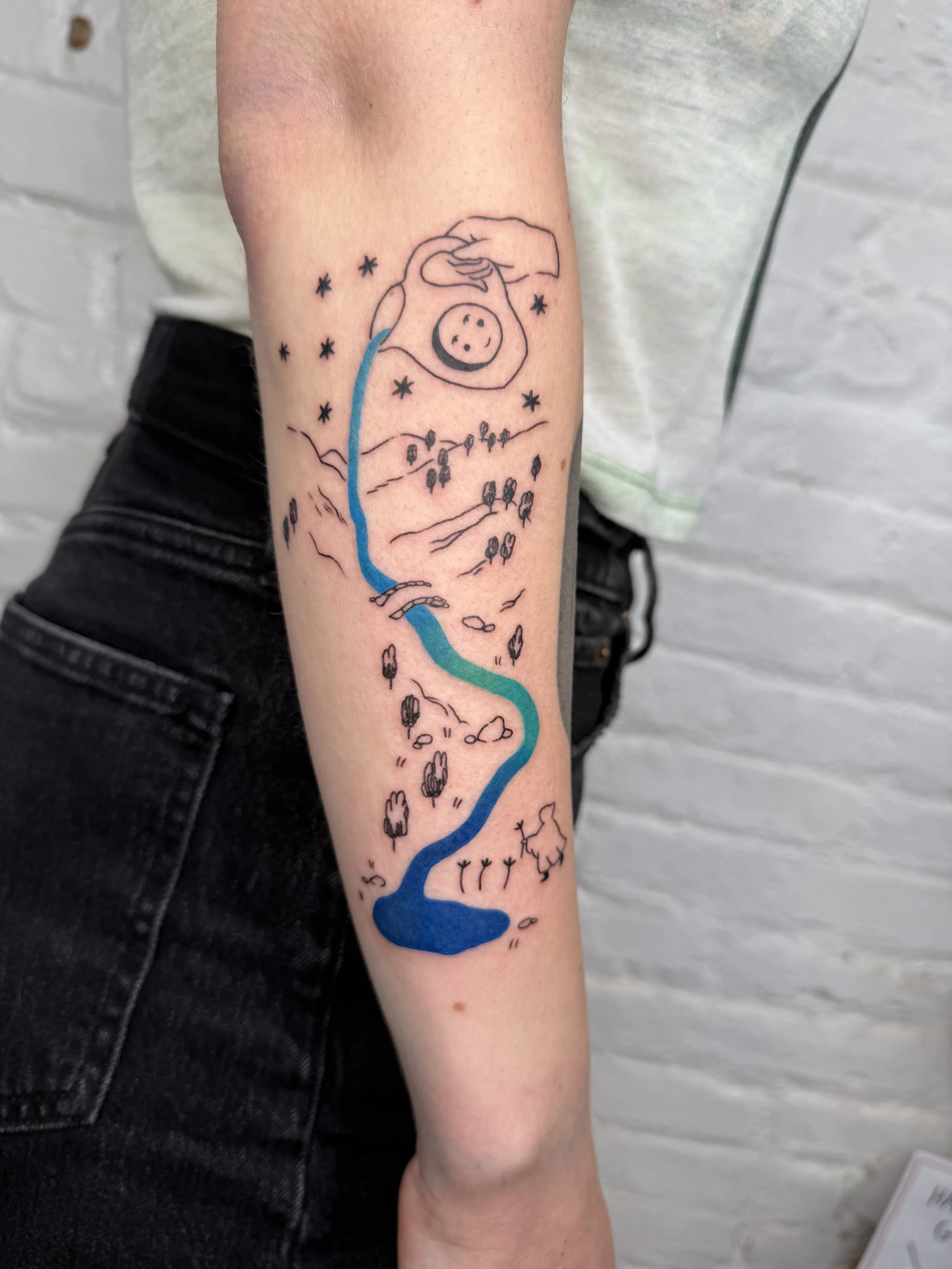 Tattoo of a landscape with a waterfall, trees, mountains, stars, a hand holding a circle with a face, and a bird on a branch.