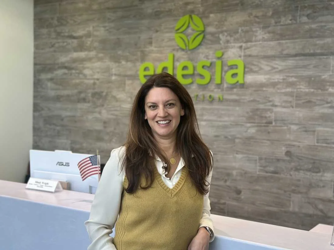A woman smiling at the reception desk of a modern office with a sign that reads 'edesia' in the background.
