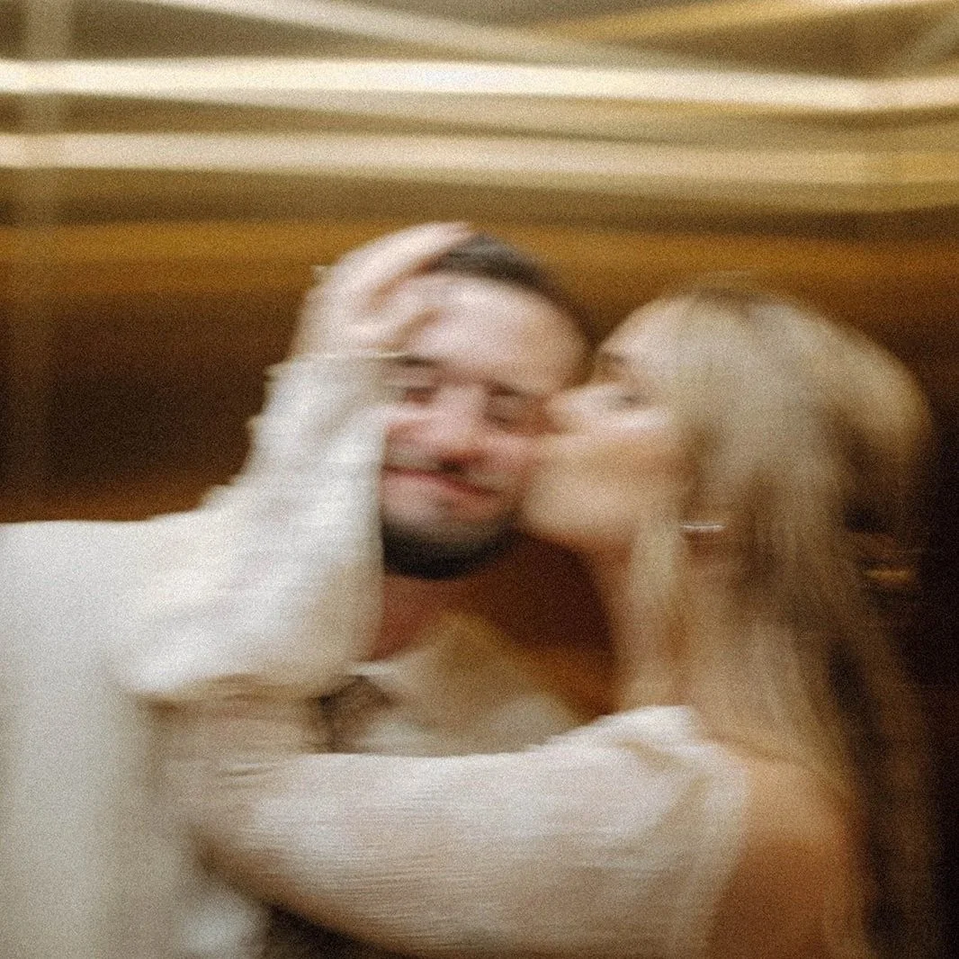 Golden blurry action shot of bride holding groom's face and kissing his cheek.