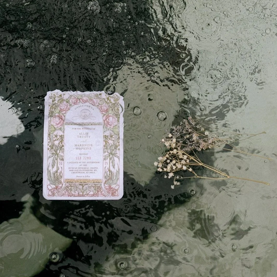 Ornate printed wedding invitation floating in body of rippled water with sprig of baby's breathe flowers