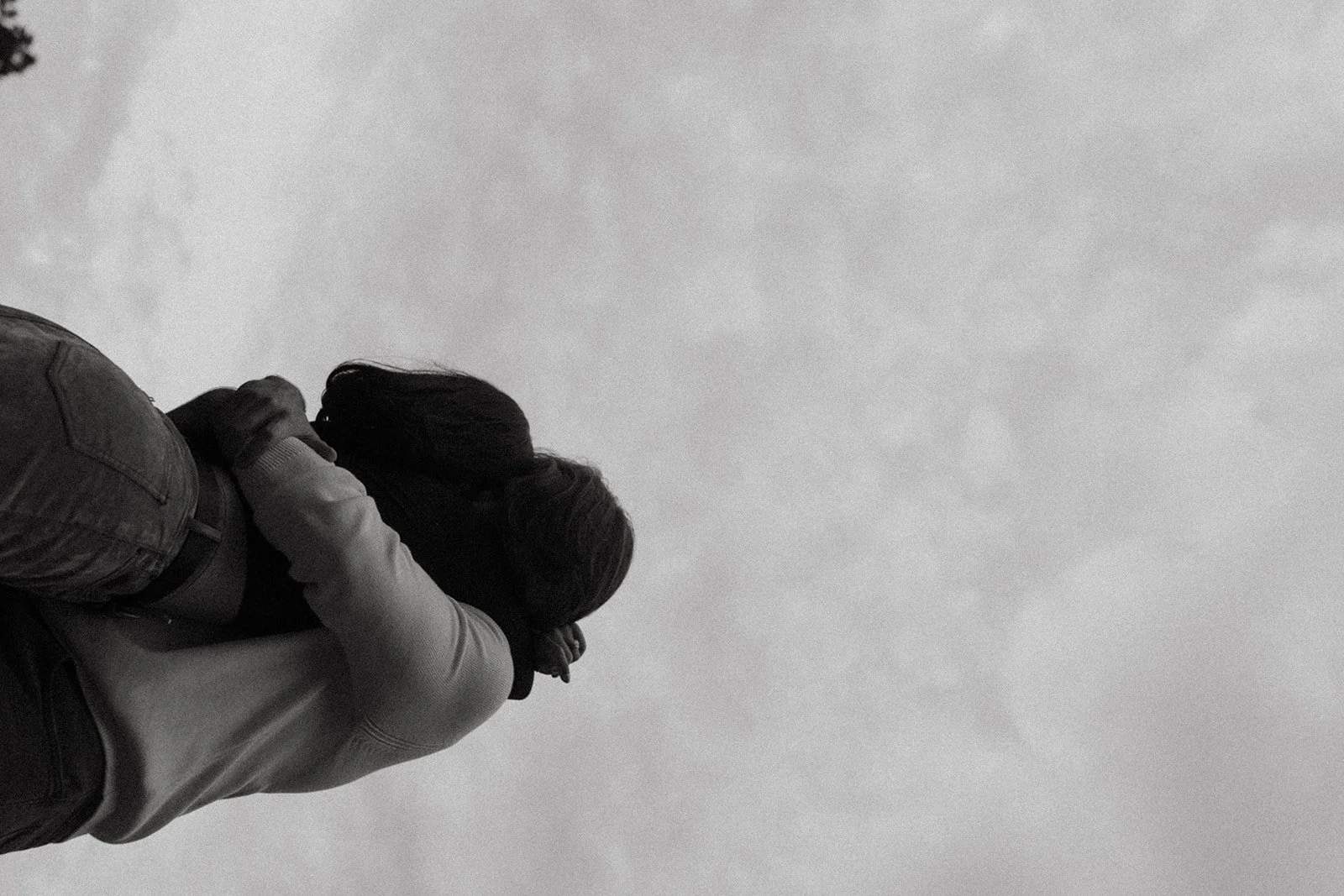 Black and white shot from ground into cloudy sky with a couple holding each other in an embrace.