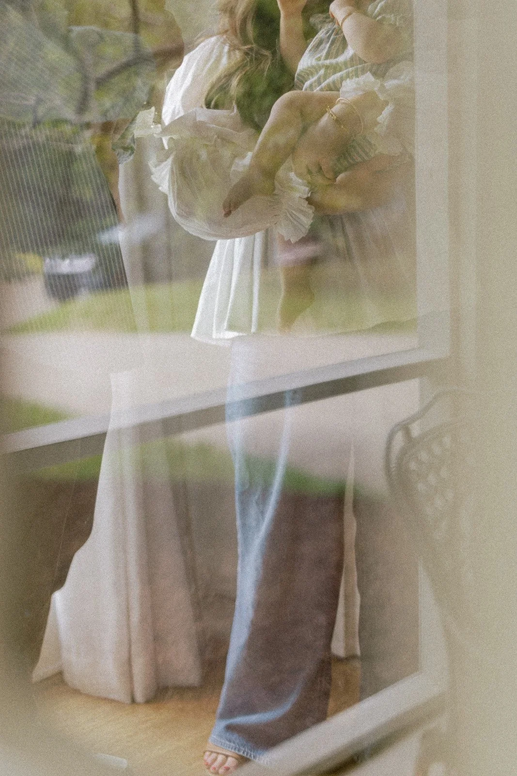 Abstract image of woman holding young child, shot through a glass door resulting in soft hues and dreamy reflections
